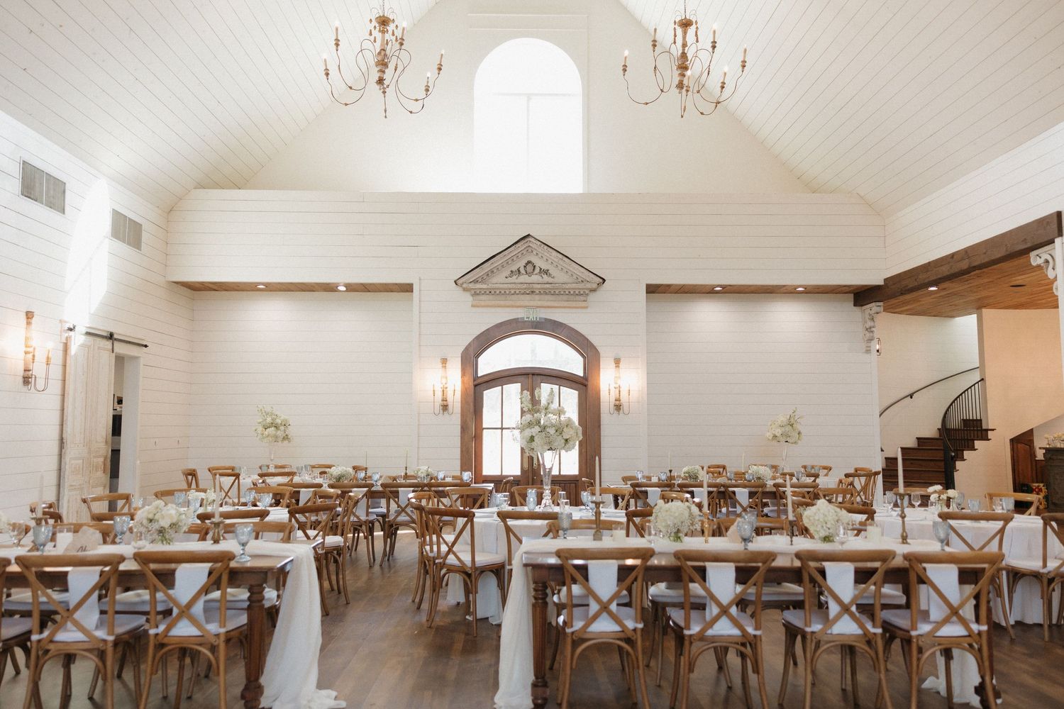 A panoramic view of an elegant wedding reception hall with white walls, chandeliers, and tables set with blue decor.
