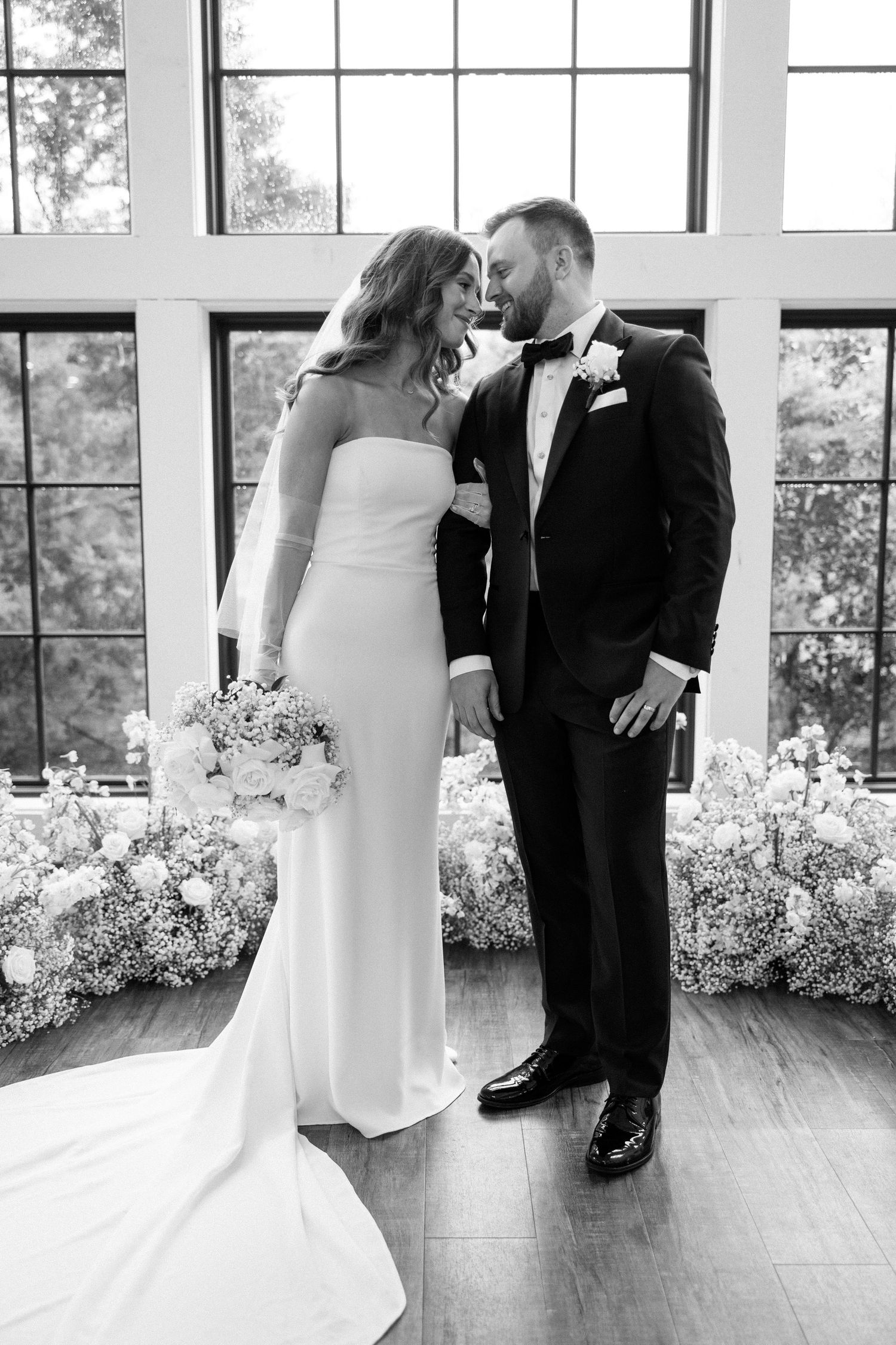 A black and white wedding photo series showing a couple dancing in an elegant room with large windows.