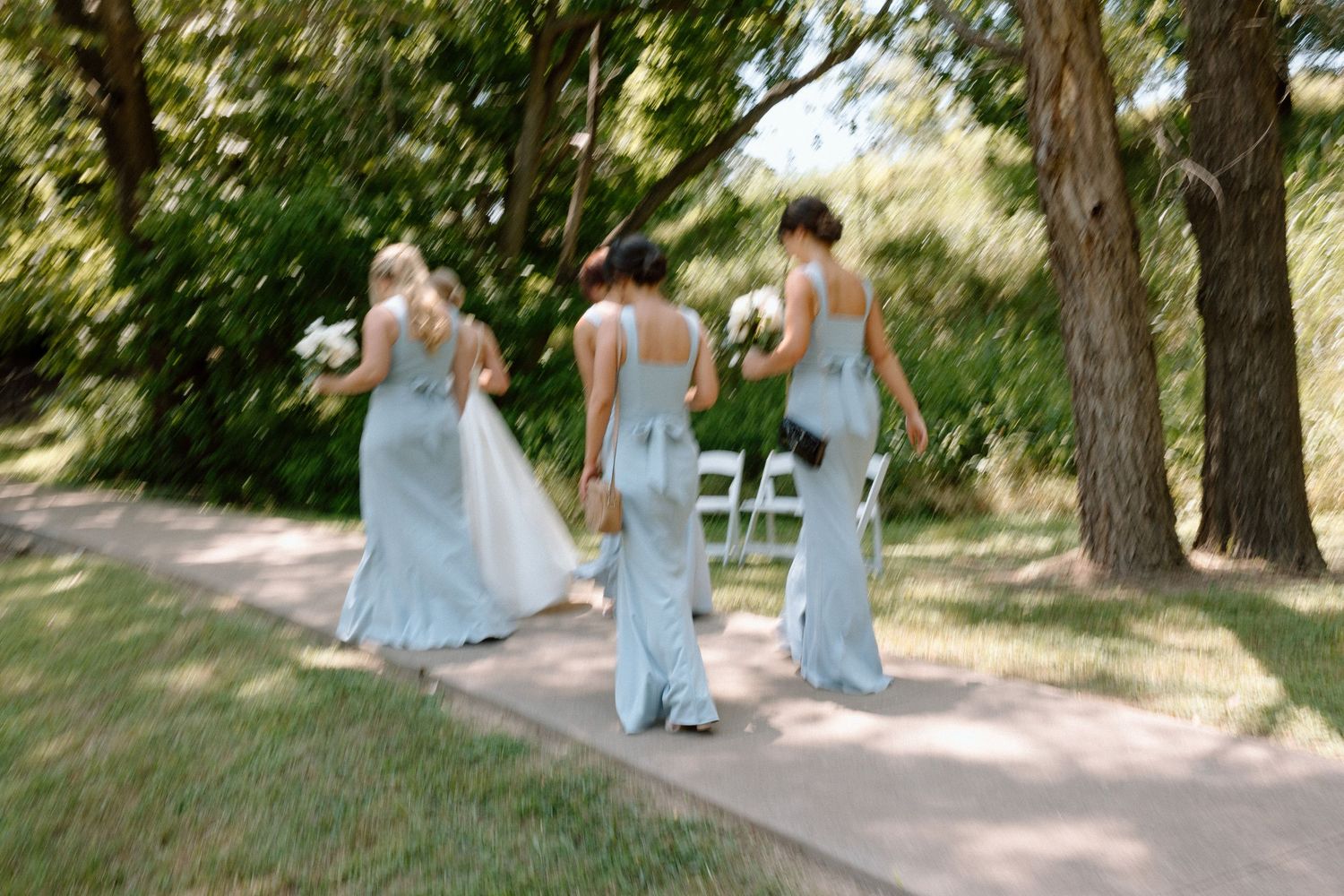 A group in light blue dresses sits together on stone steps in a sunny outdoor garden setting.