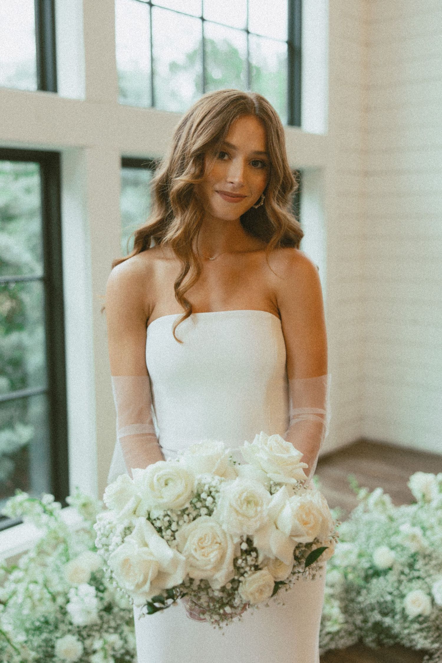 A bride in a strapless white wedding dress holds an elegant bouquet of white roses and baby's breath.