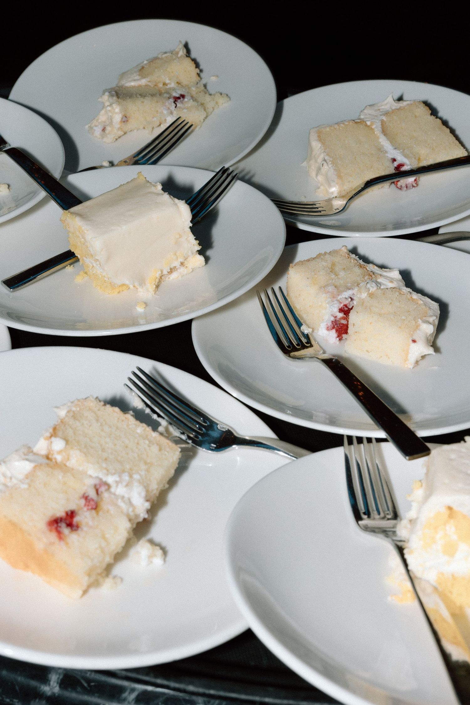 Several slices of creamy white tres leches cake with red fruit garnish served on white plates with silver forks.