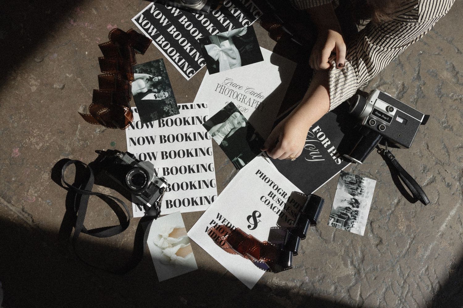 Scattered black and white fashion marketing materials and shoes arranged on concrete floor with hands styling.