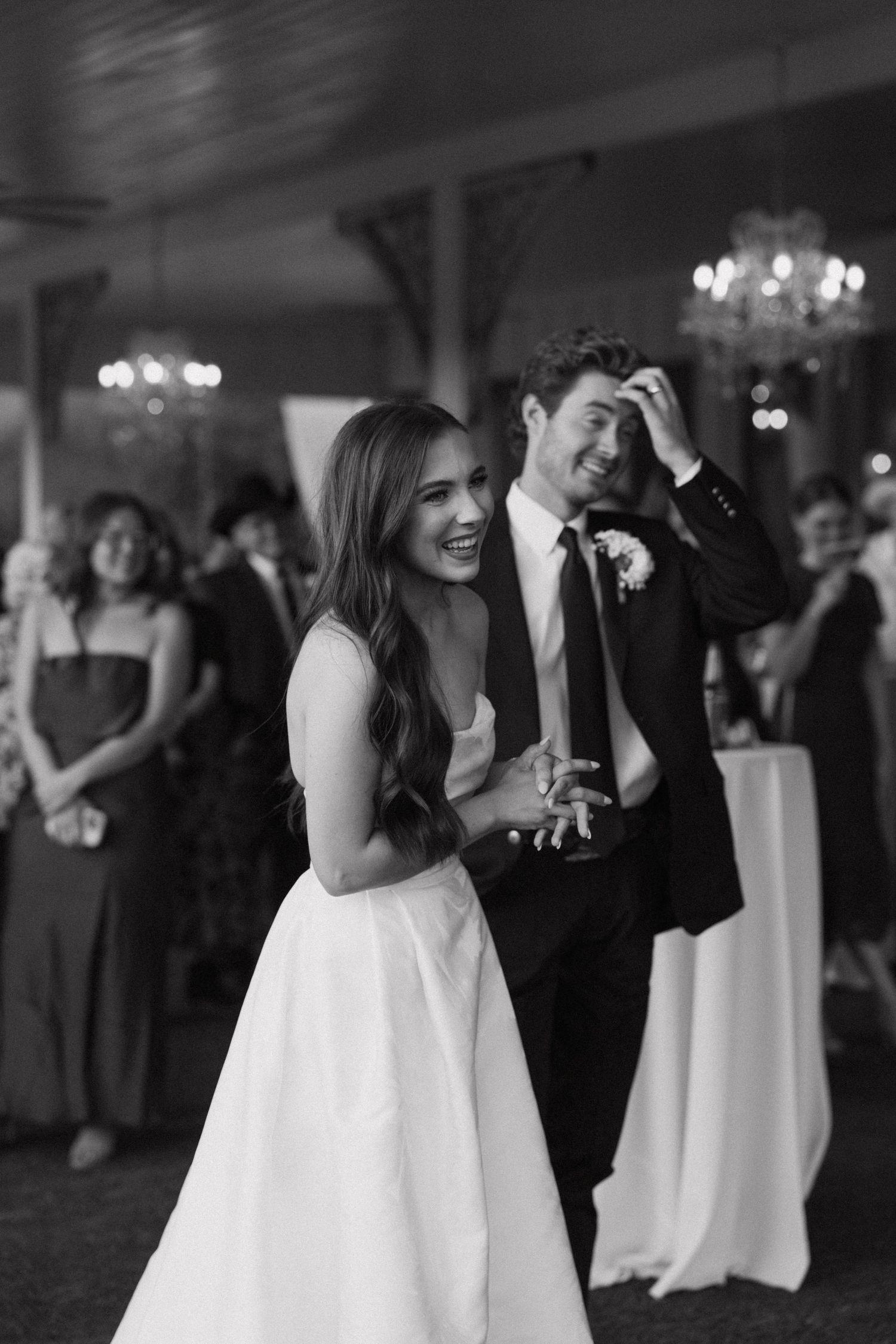 Wedding guests dancing and celebrating at an elegant reception with chandeliers and formal attire.