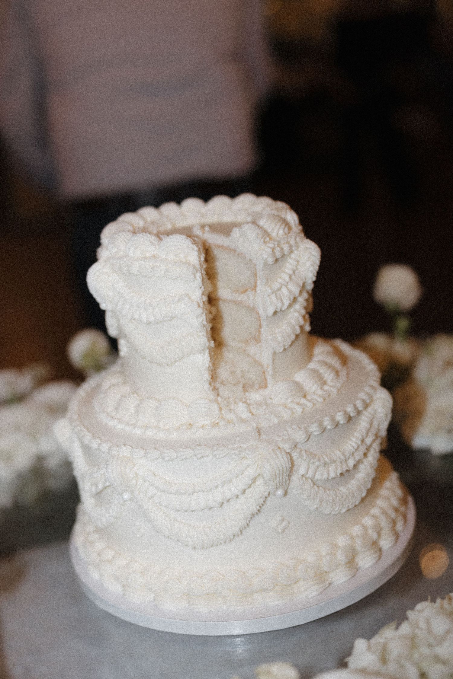 A close-up view of an elegant white wedding cake with delicate piped details and pearl decorations on display.
