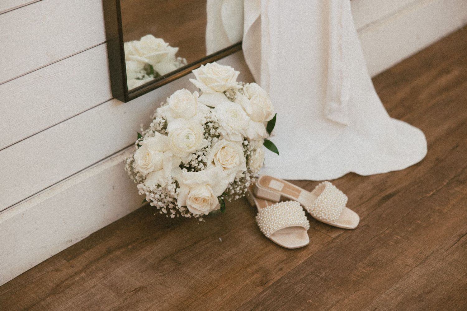 White floral arrangements and wedding dress details sit elegantly on a light wooden floor.