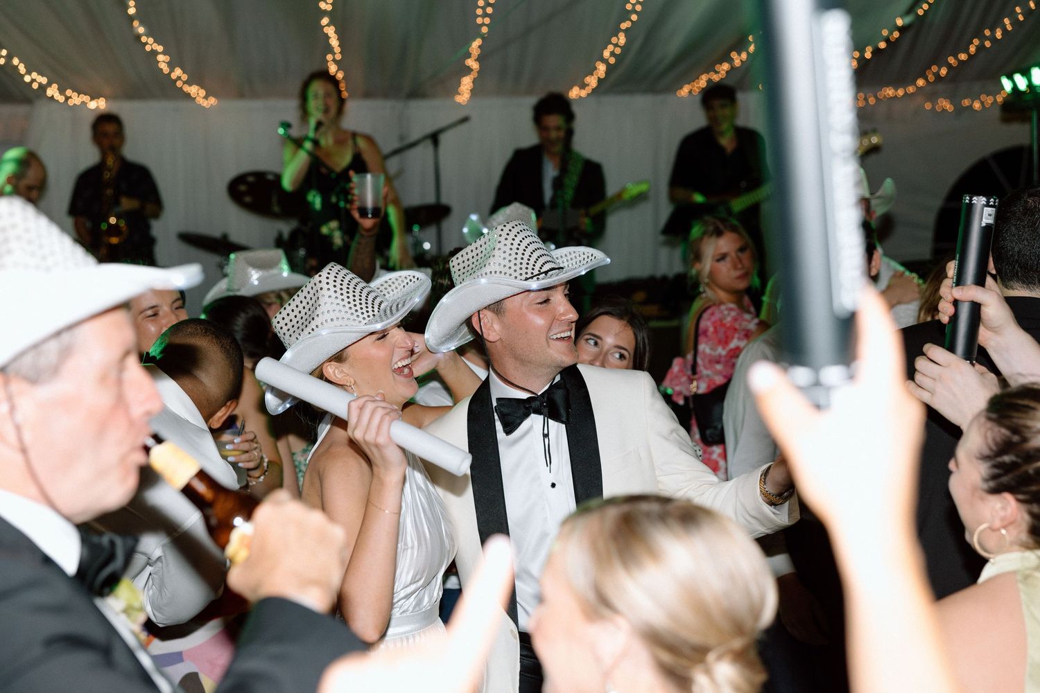 Crowd of wedding guests dancing and celebrating on a dance floor decorated with string lights overhead.