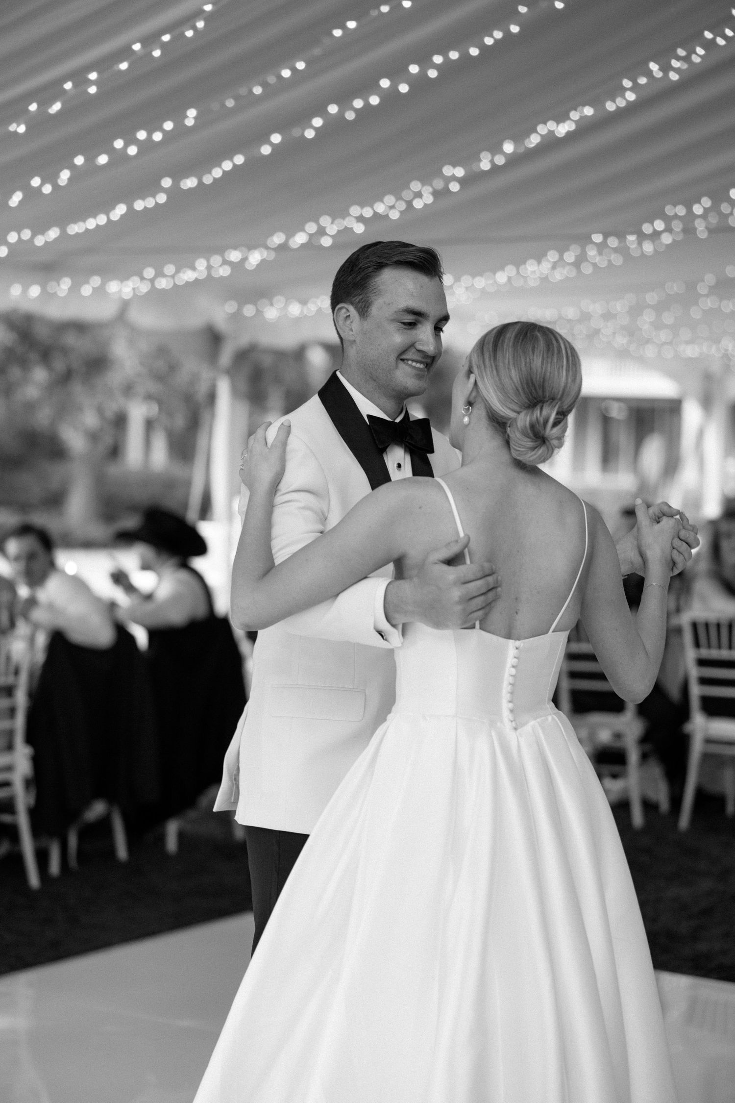 A couple shares an intimate dance moment under twinkling string lights at their wedding reception.