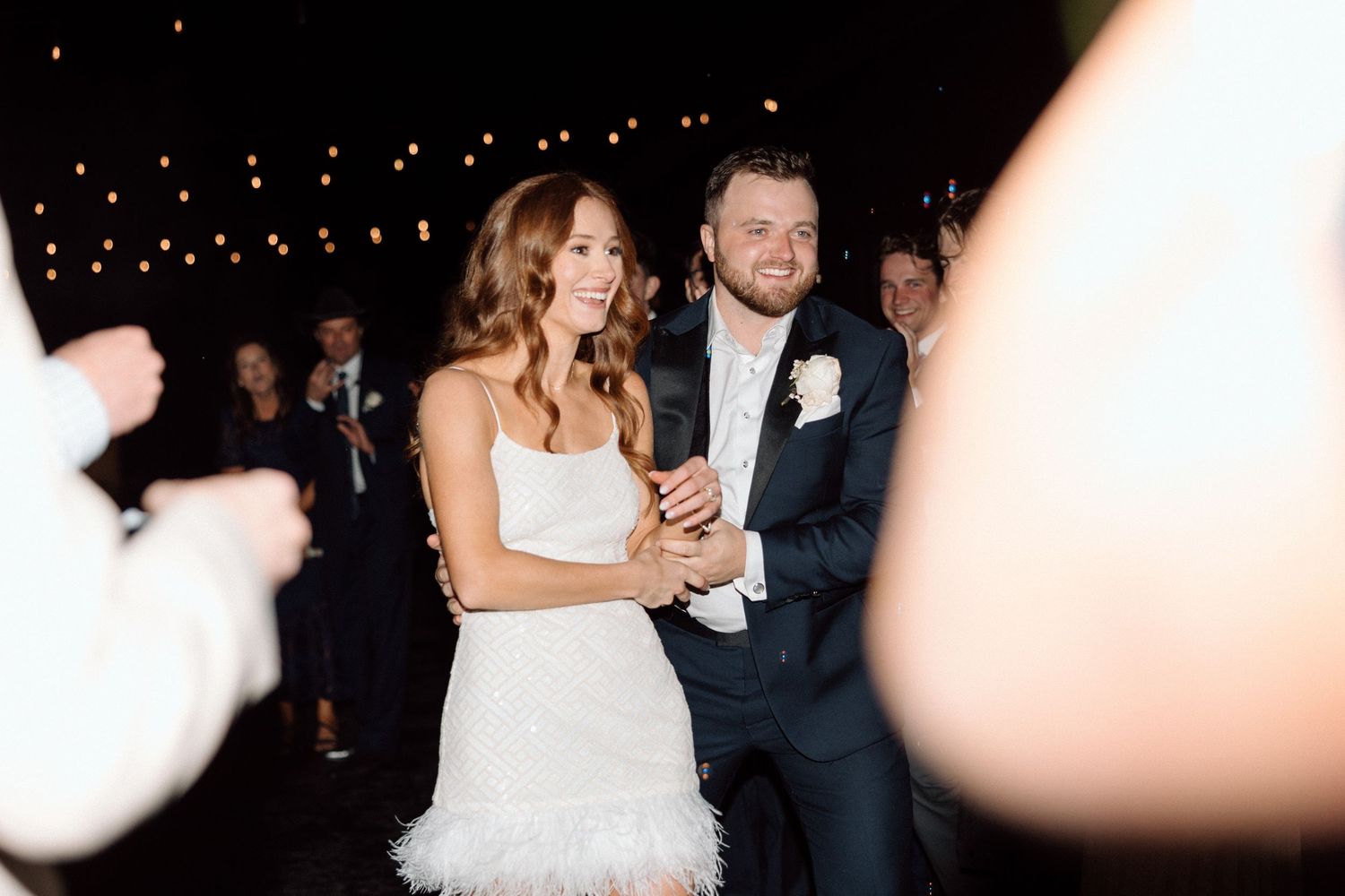 A wedding couple and their guests dance and celebrate together on a dimly lit dance floor at a reception.