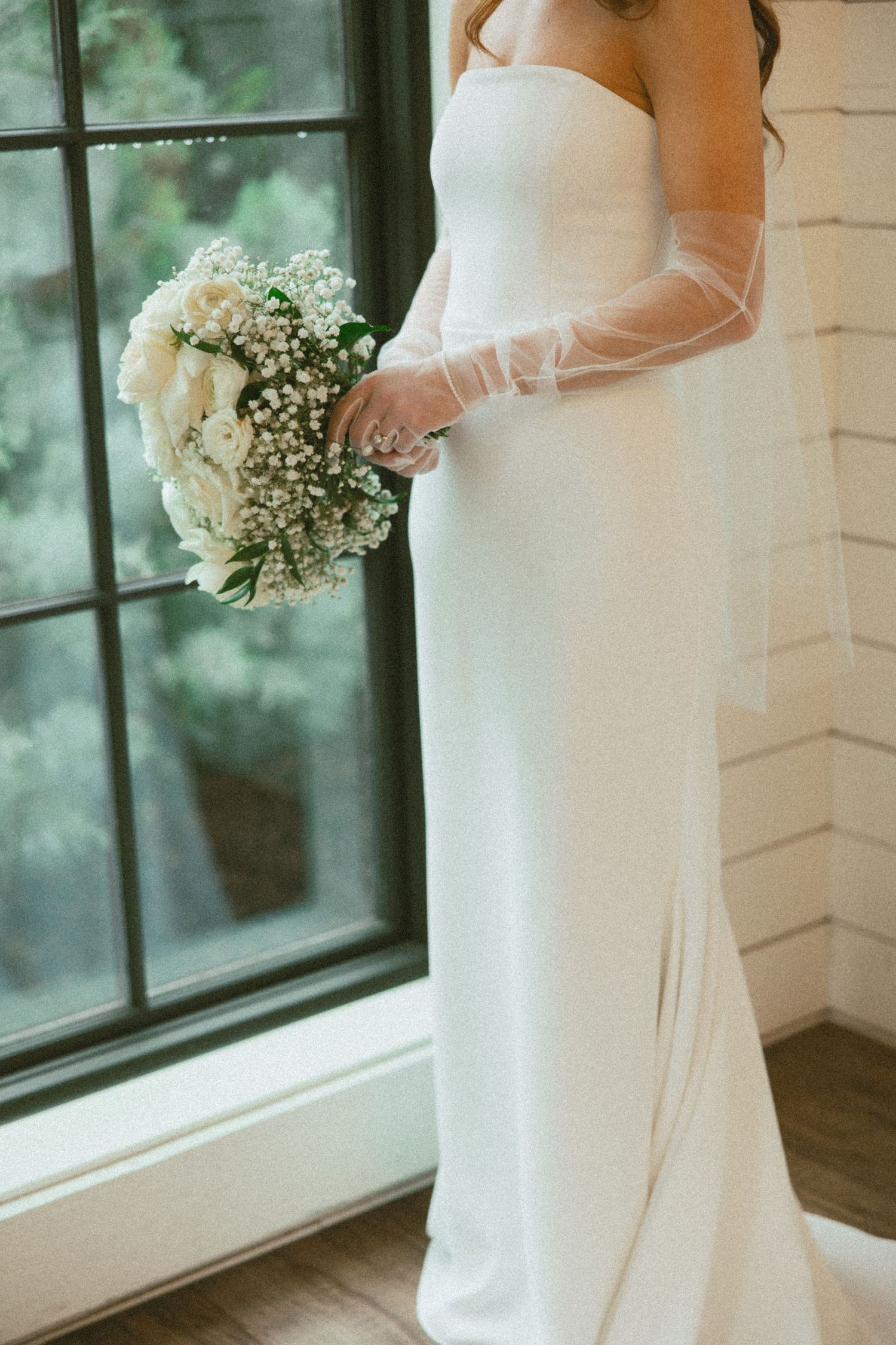 Elegant white wedding dress detail shots showing flowing fabric and delicate baby's breath bouquet near window.