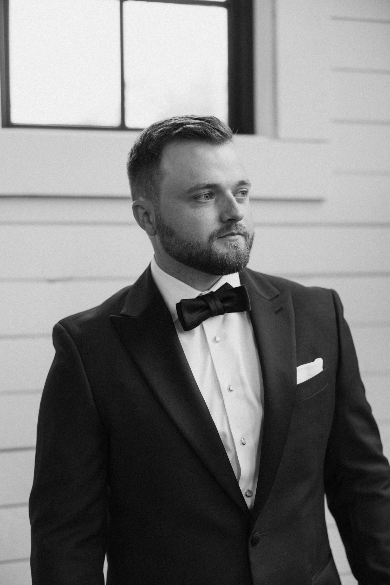 A black and white photo series showing different angles of a groom in a formal tuxedo and bow tie.