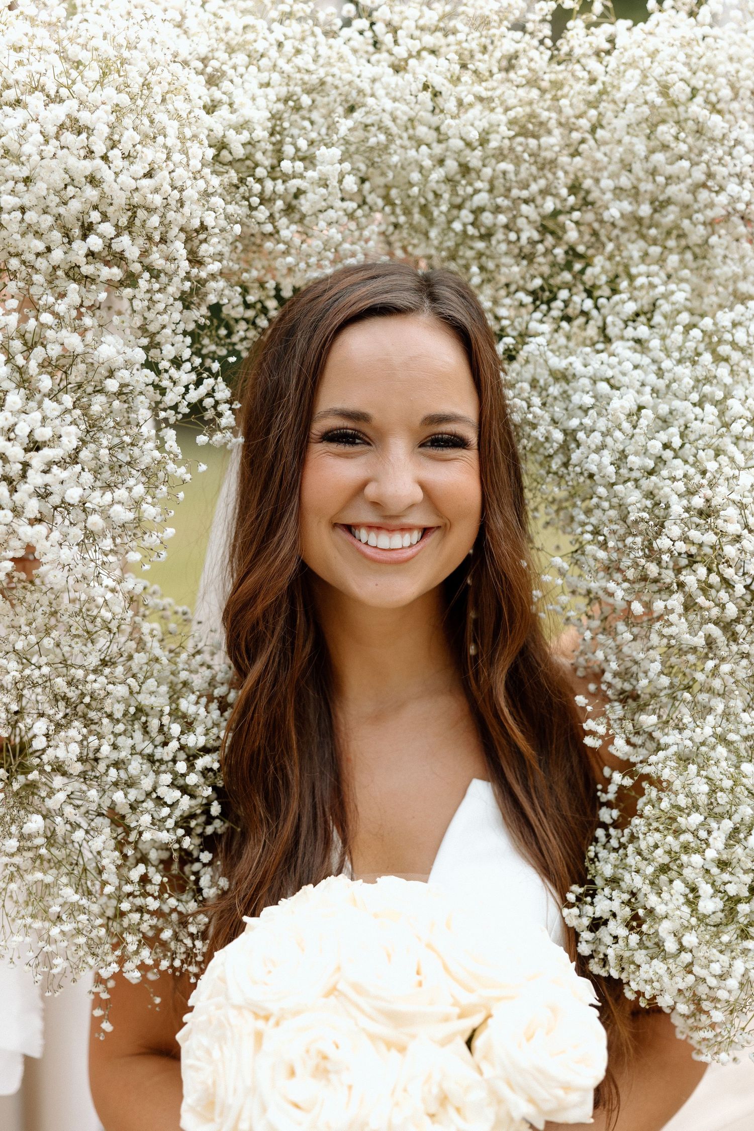 Portrait of someone in a white top surrounded by delicate white baby's breath flowers on a sunny day.