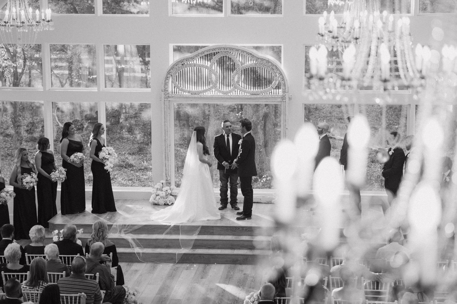 Black and white collage of elegant wedding ceremony moments in a grand ballroom with chandeliers and floral decor.