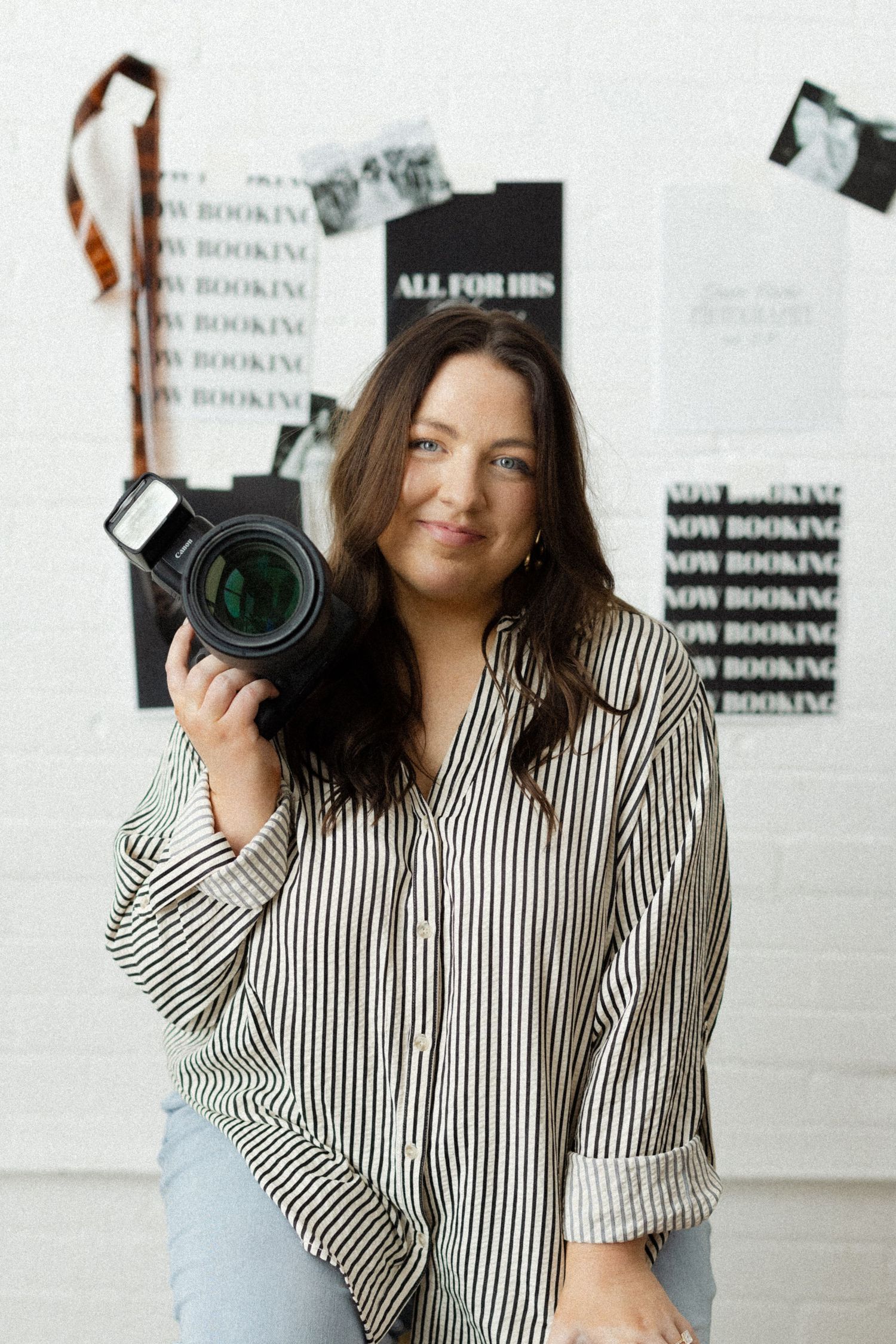 Professional photographer in striped shirt holding camera in studio with white backdrop.
