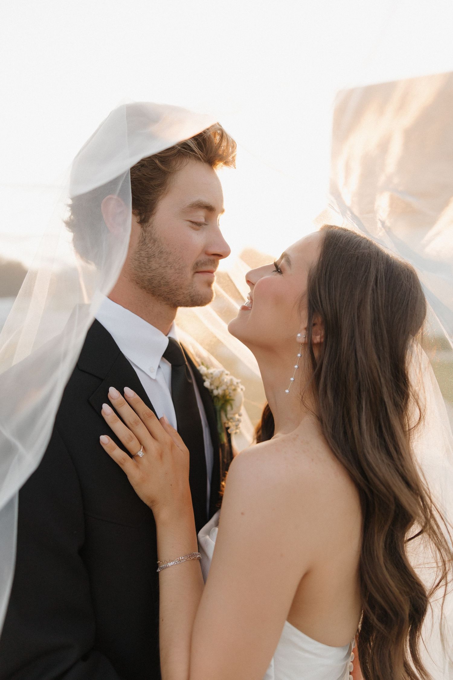 A romantic wedding couple embraces in soft golden sunlight during their sunset photoshoot.