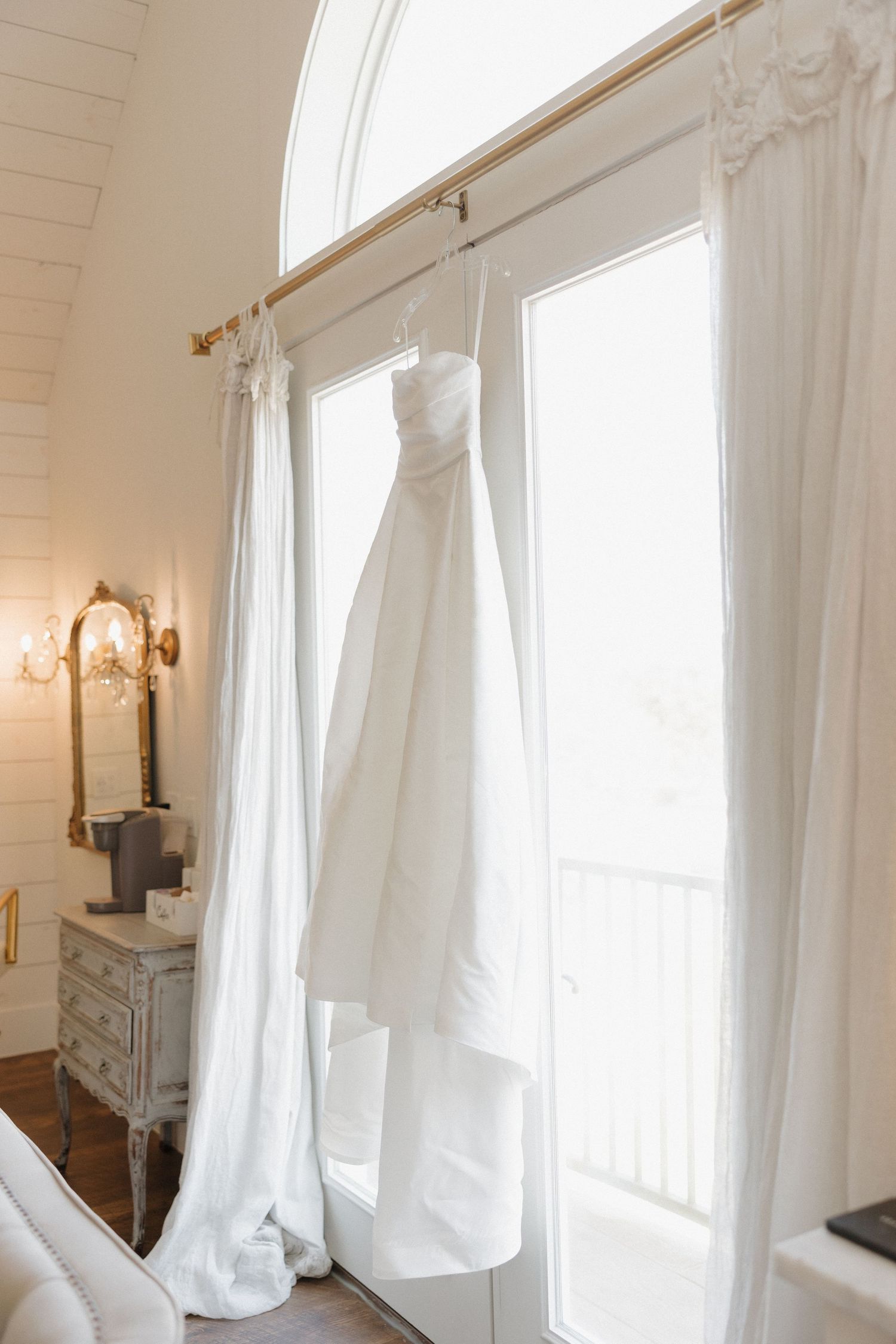 Elegant white curtains billow near tall windows in a bright room with wall sconces and vintage-style decor.