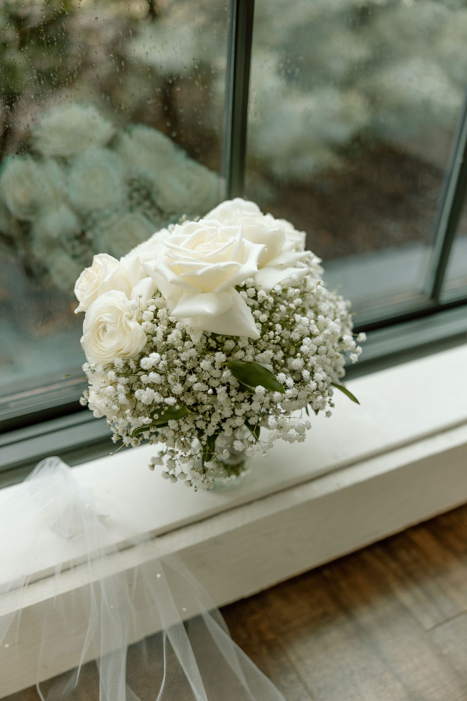 A delicate white rose bouquet with baby's breath sits on a windowsill, creating an elegant wedding arrangement.