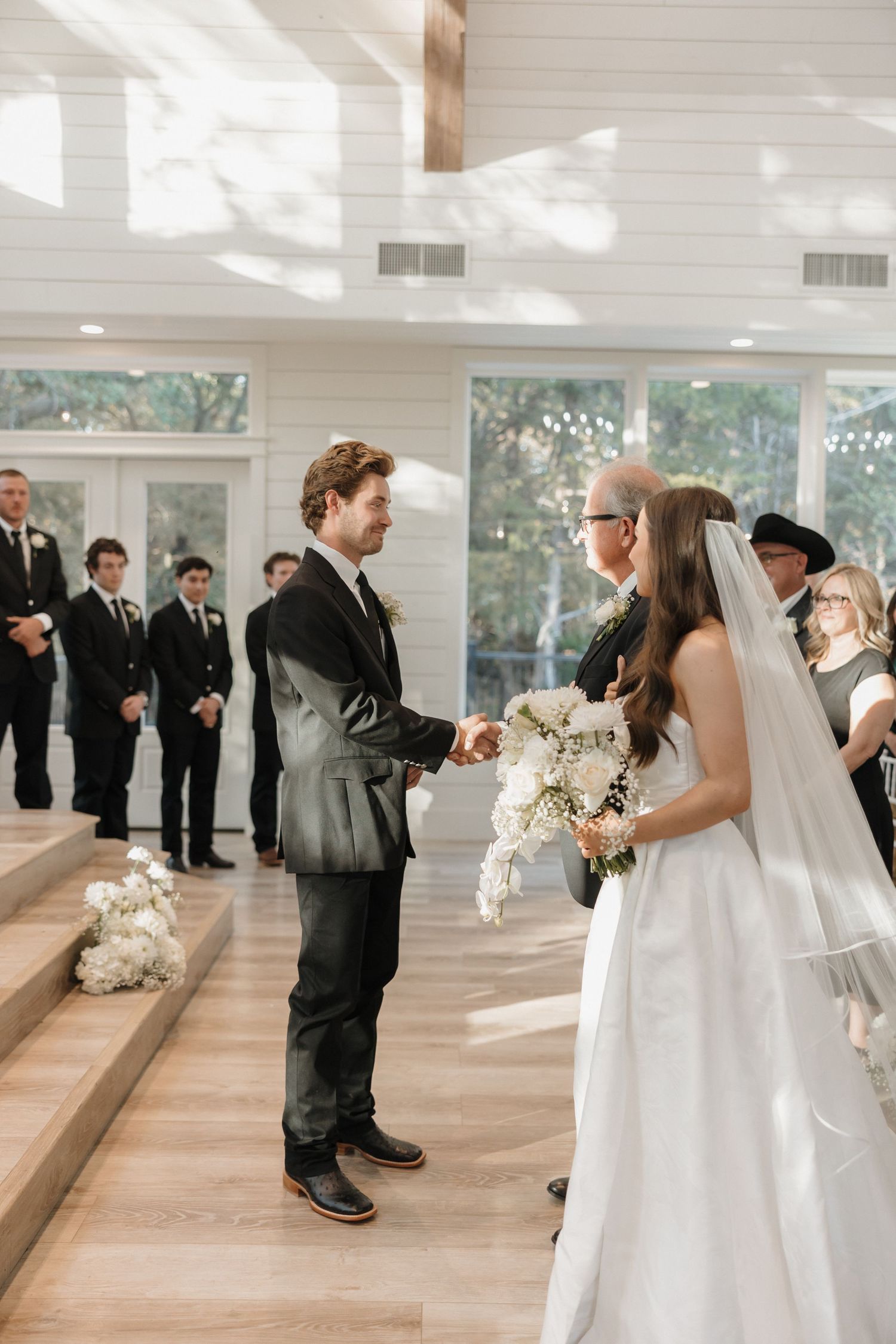A wedding couple shares their first look moment in a bright indoor venue with light wood floors and white walls.