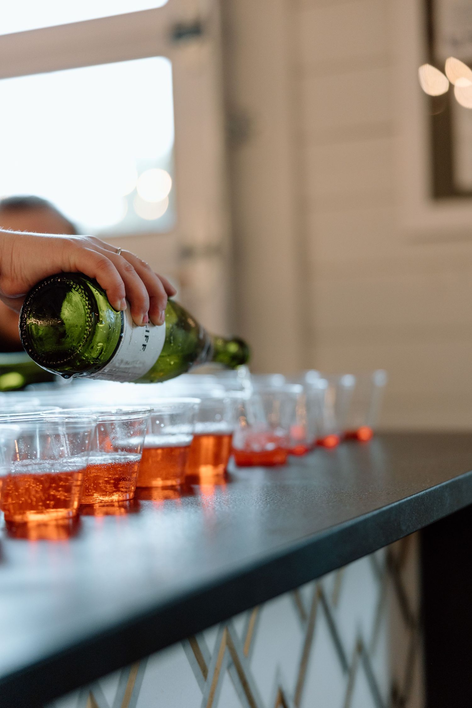 A row of champagne glasses being filled with pink sparkling wine from a bottle in a dimly lit setting.