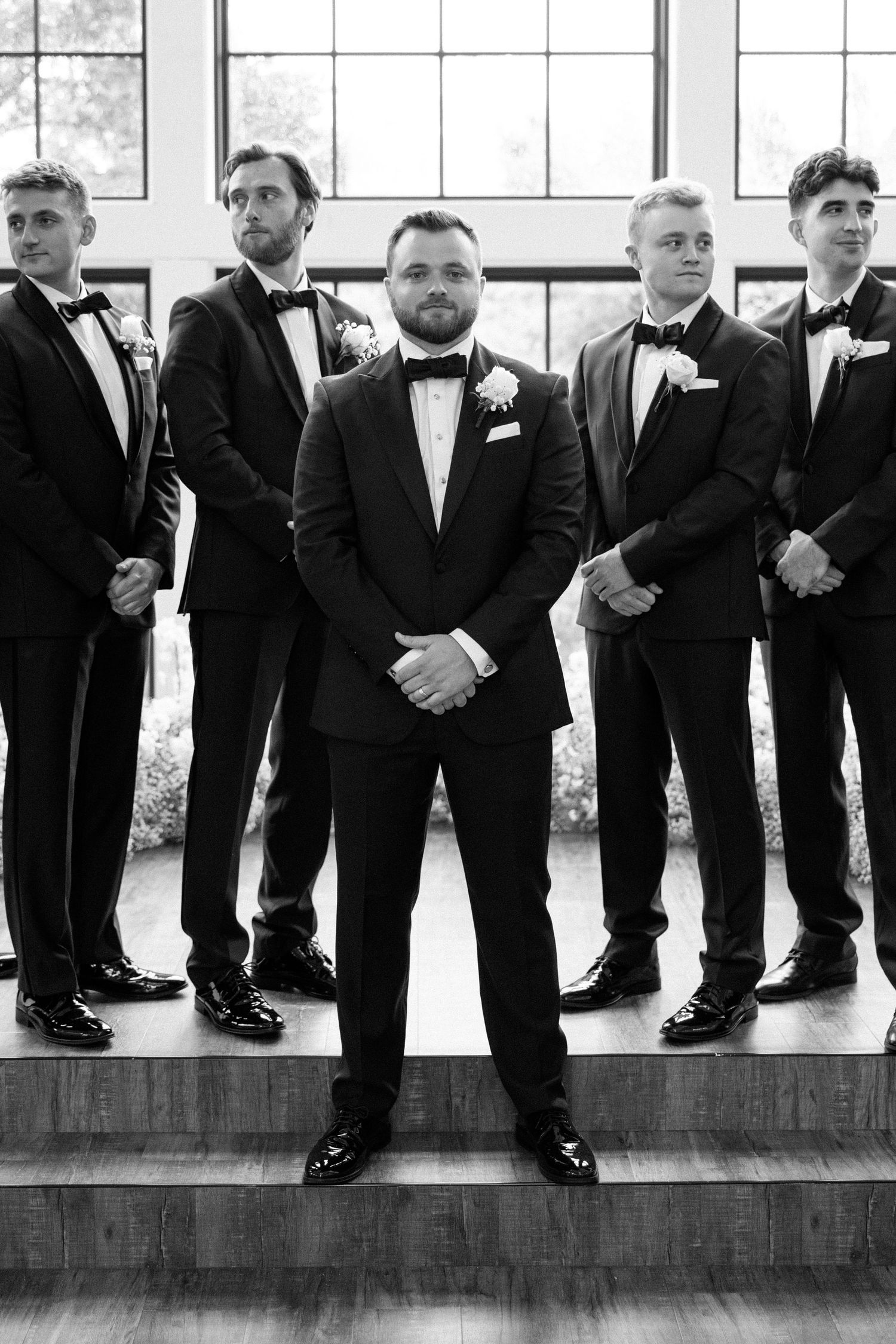 Creative black and white photo showing groomsmen's legs and dress shoes lined up against a window.