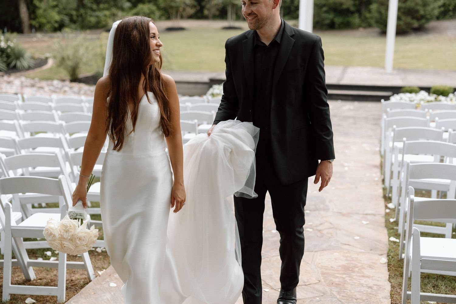 A bride and groom share a romantic moment together during their outdoor wedding ceremony surrounded by white chairs.