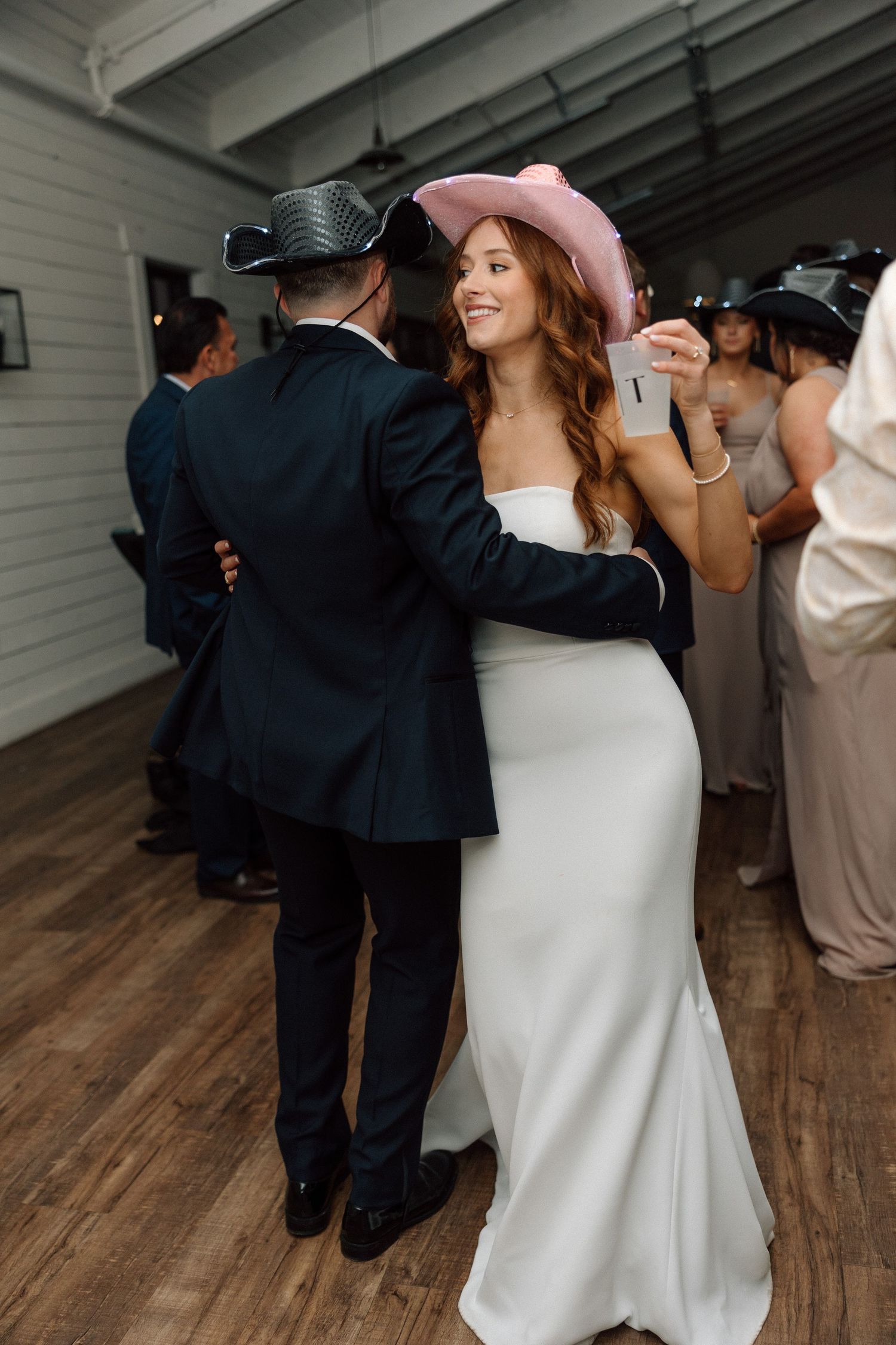 A couple shares an intimate dance moment at their wedding reception on a wooden floor.