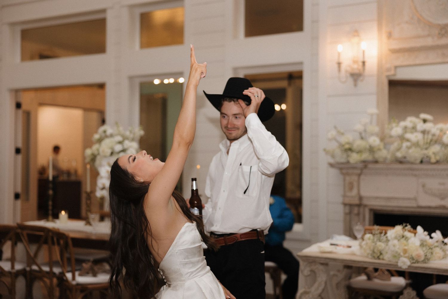 A couple dances joyfully at their wedding reception in an elegant venue with white floral decorations.