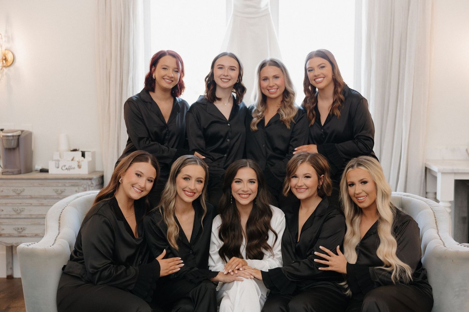 A group wearing matching black robes poses together in an elegant white room with ornate decor.