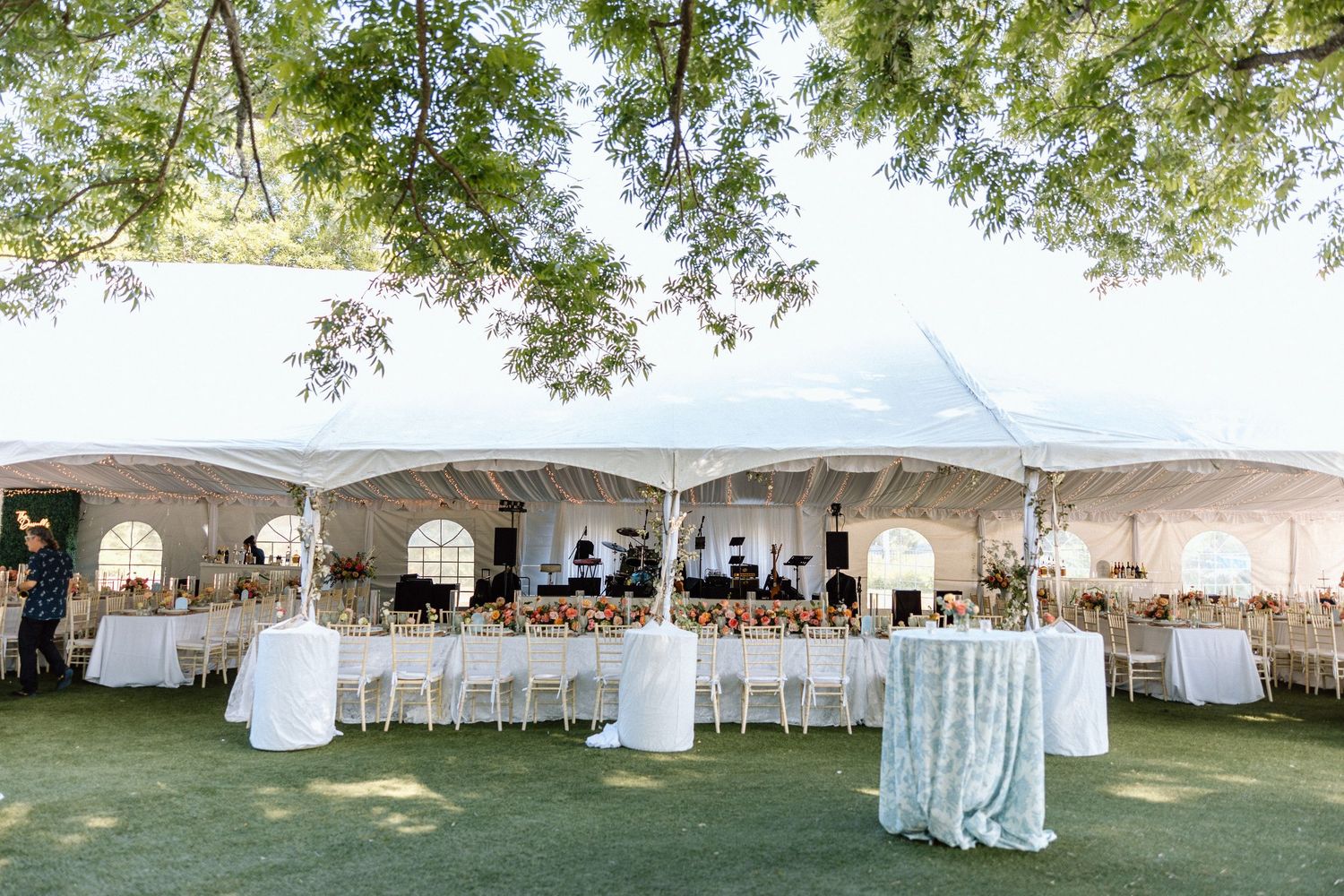 A row of white wedding tents set up outdoors with tables and chairs arranged underneath for a garden reception.