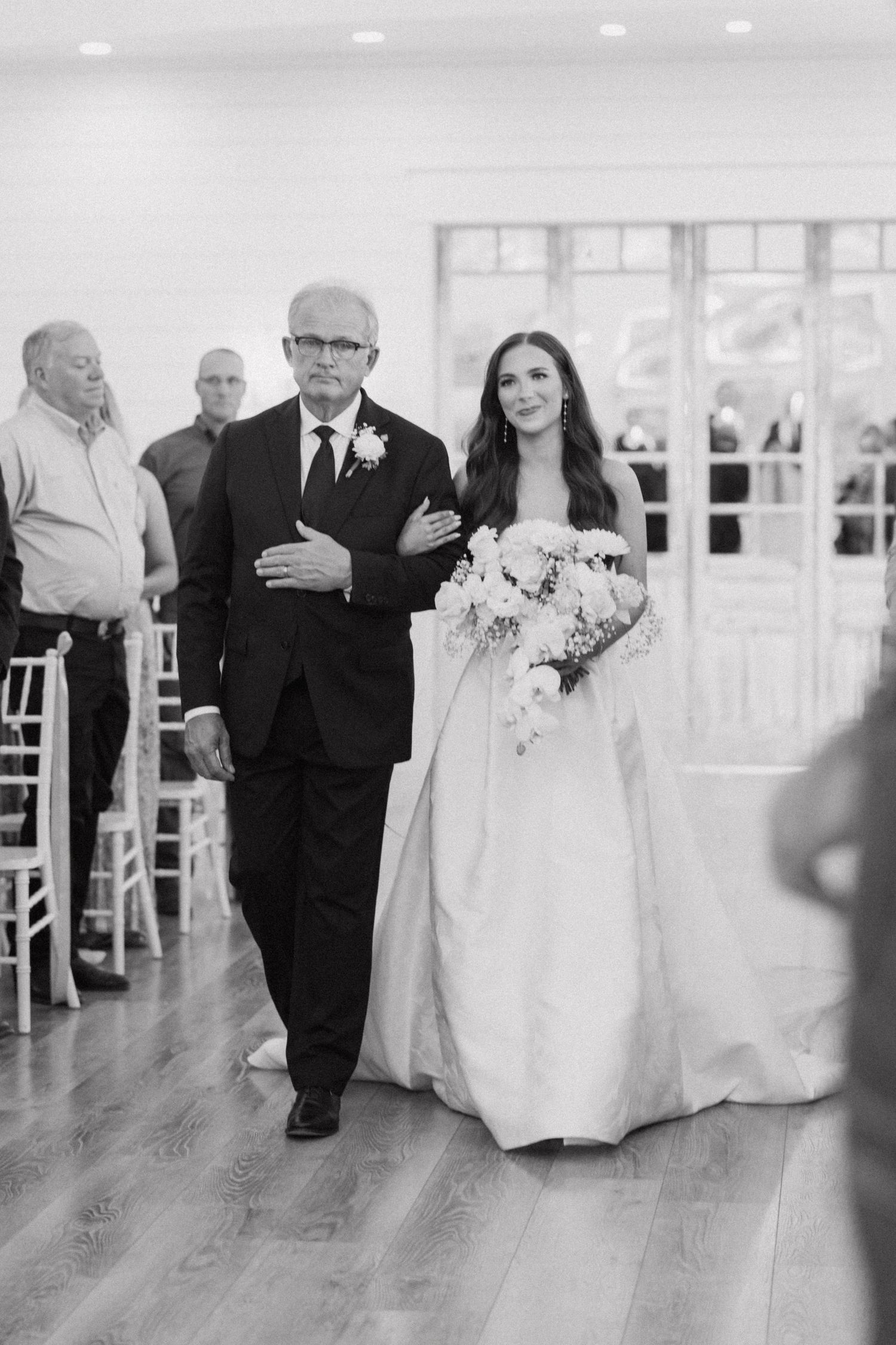 Black and white wedding reception photo showing dancing couples on a hardwood floor at an elegant venue.