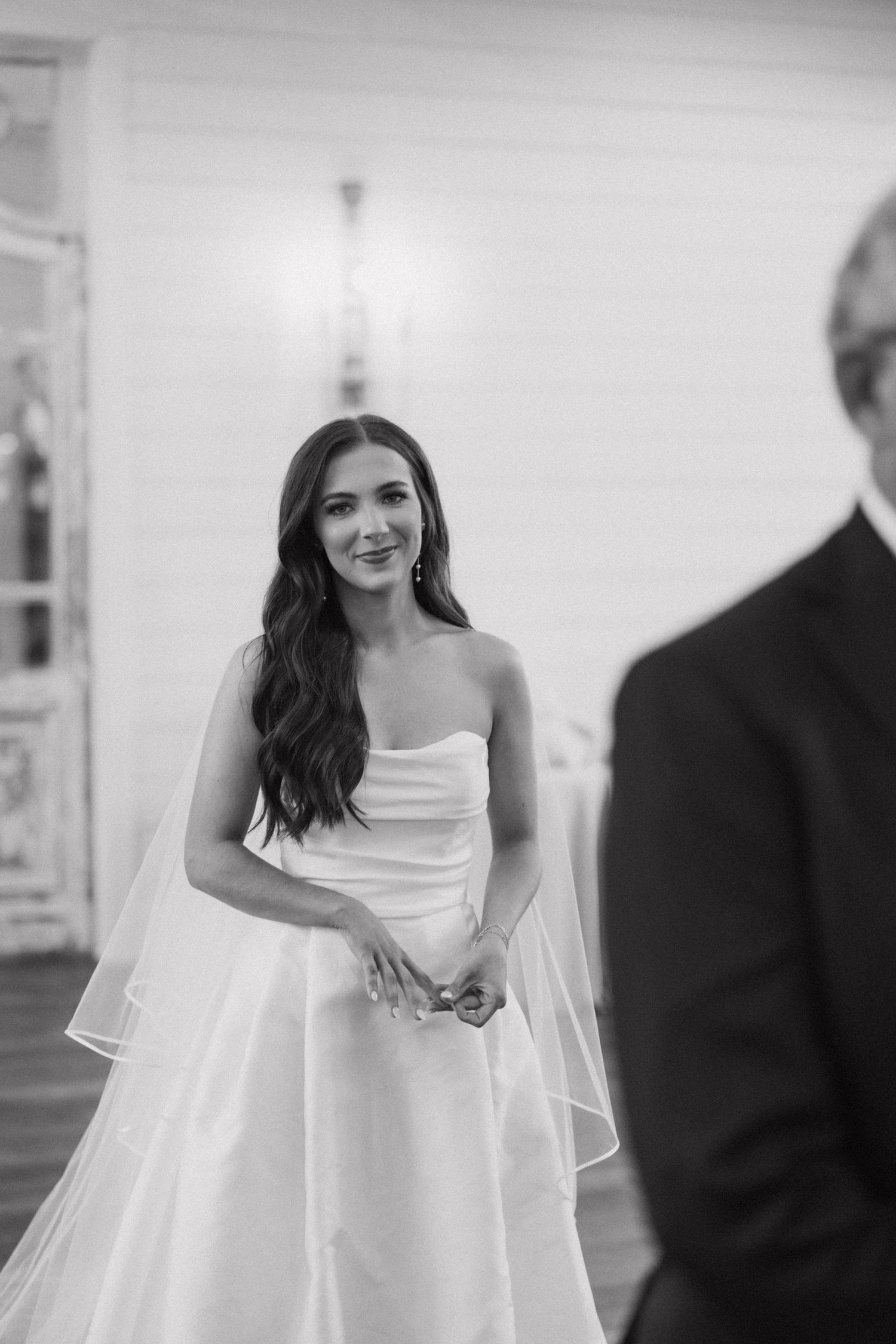 A bride in a strapless white wedding gown with long veil smiles during her wedding ceremony.