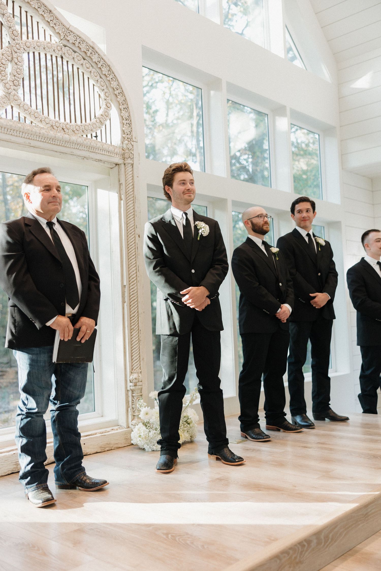 Creative wedding photo showing groomsmen's legs and shoes lined up in black suits against a bright white interior.