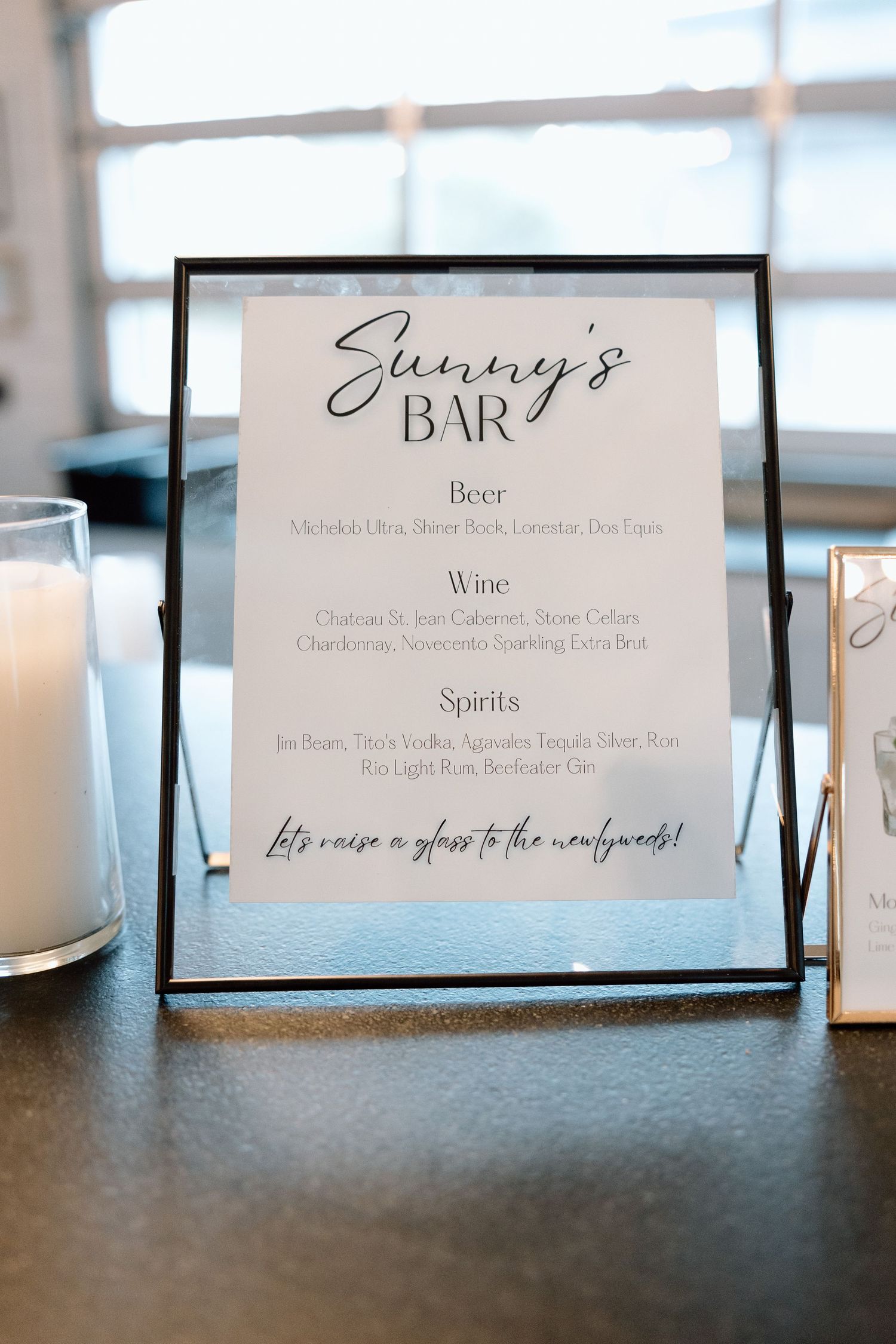 Elegant framed bar menu displaying 'Sunny's Bar' with wine and spirits offerings on a dark surface with candles.