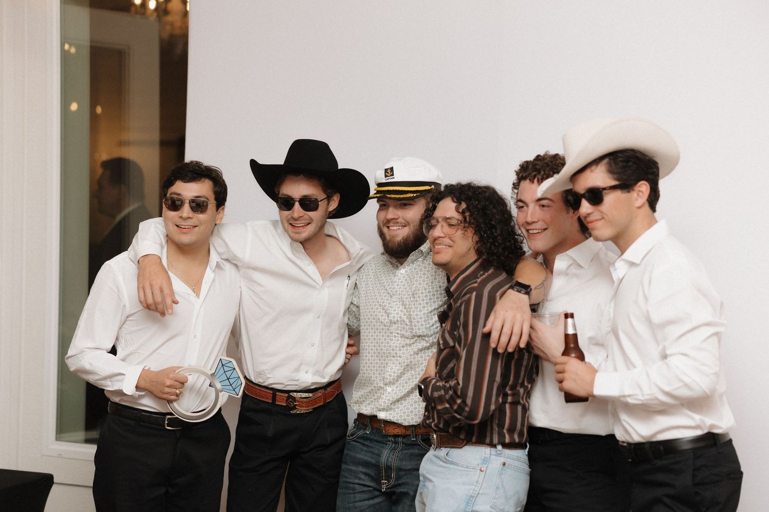 A group of people in formal attire stand together in a line with arms around each other's shoulders.