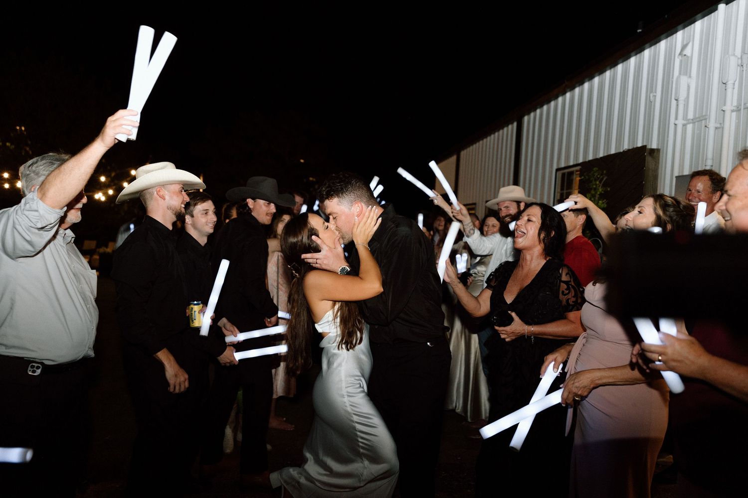Wedding guests hold glowing white light sticks during a nighttime celebration send-off.