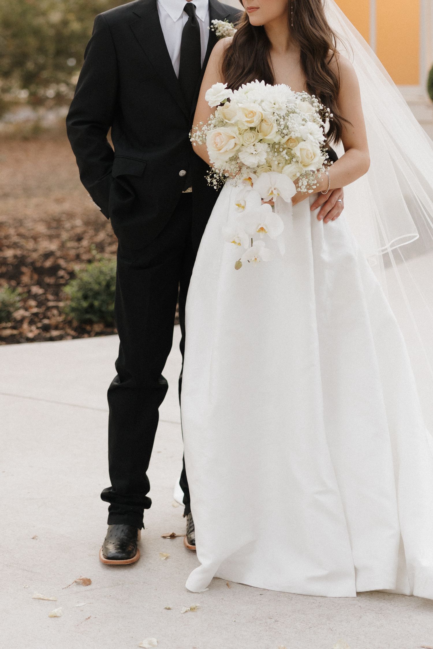 Wedding couple's feet shown in formal attire with white dress and black shoes against light colored floor.