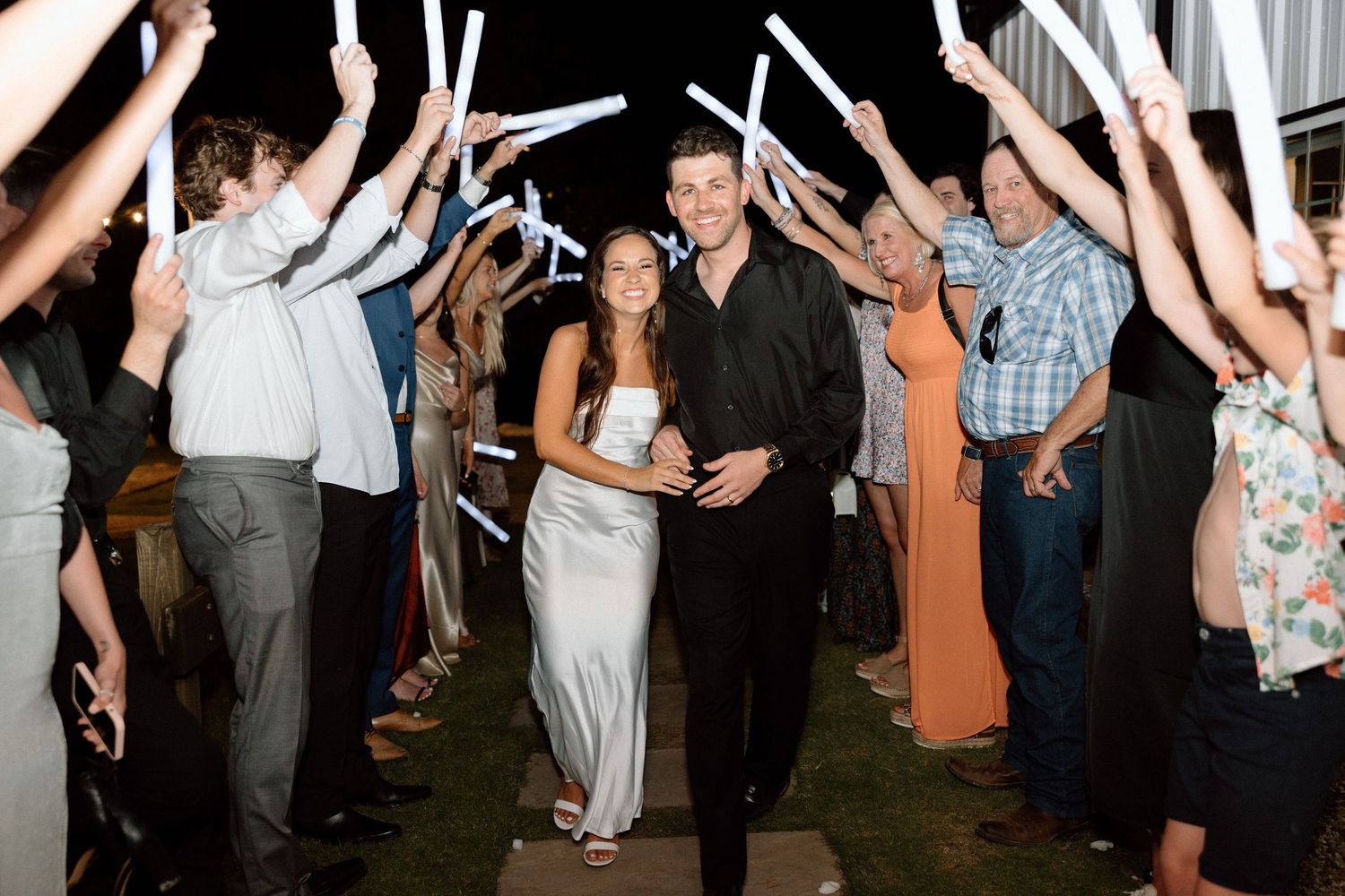 Wedding guests form a tunnel with raised arms for the newlyweds to walk through during an evening reception celebration.