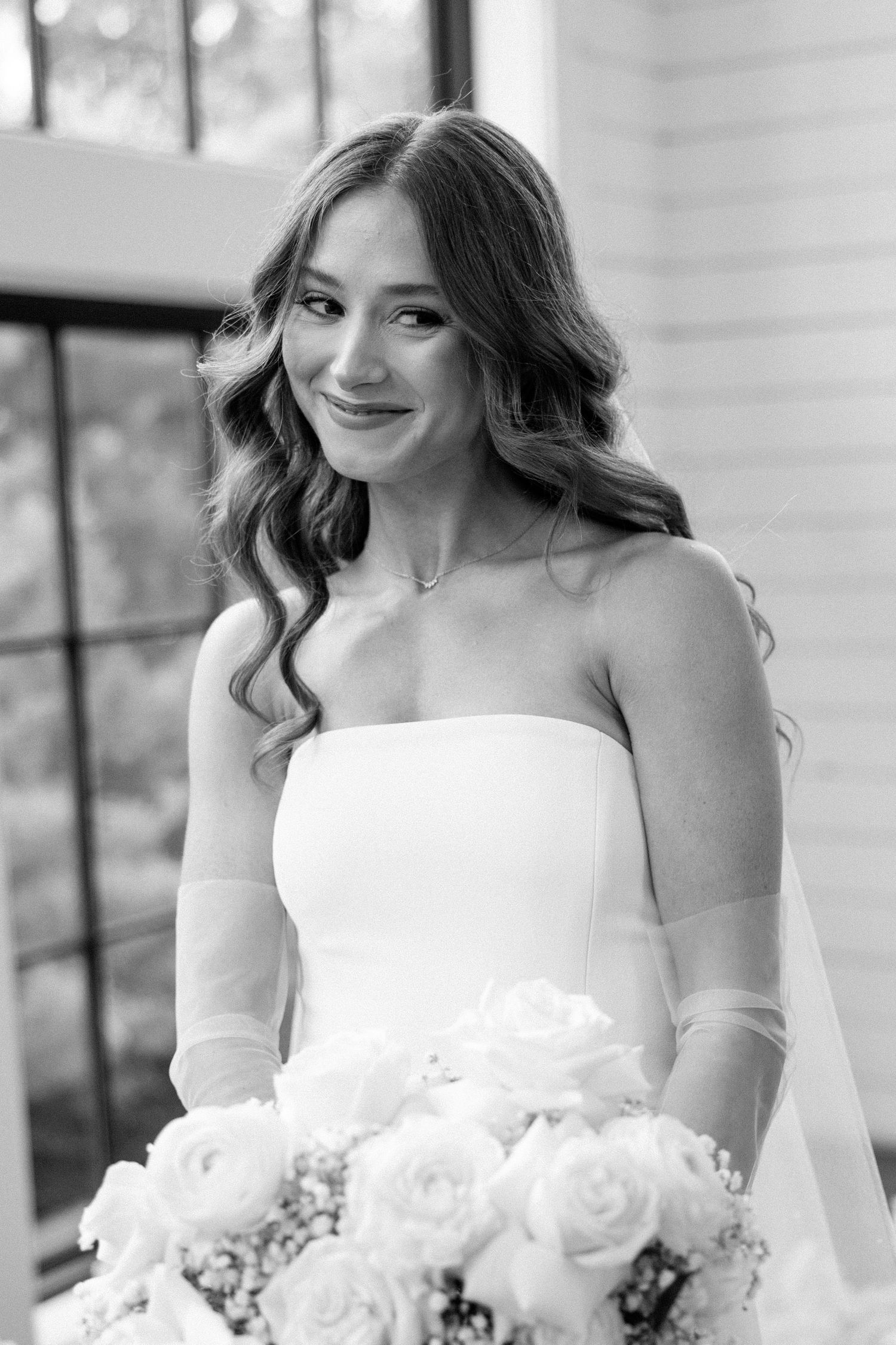 A bride in a strapless white wedding gown holds a bouquet of white roses while smiling in a series of black and white photos.