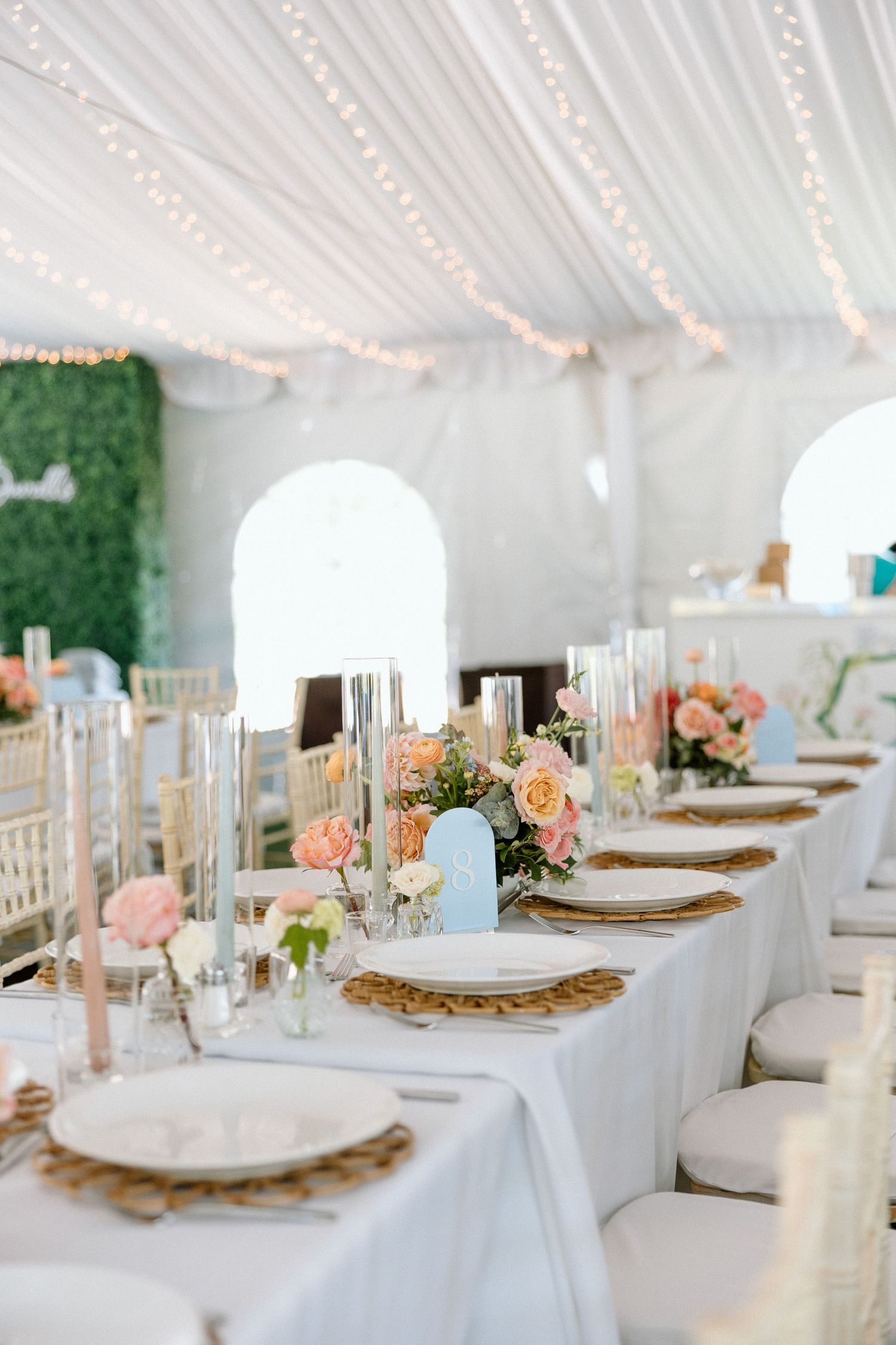 Elegant wedding reception table setting with white linens, gold chargers, peach roses and twinkling string lights overhead.