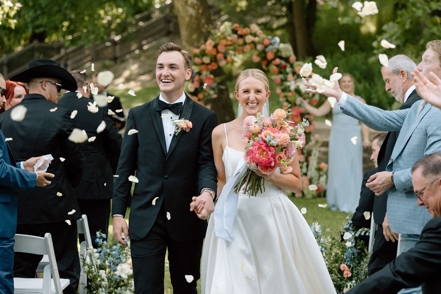 Newlyweds celebrate with guests throwing white confetti during an outdoor garden wedding ceremony.