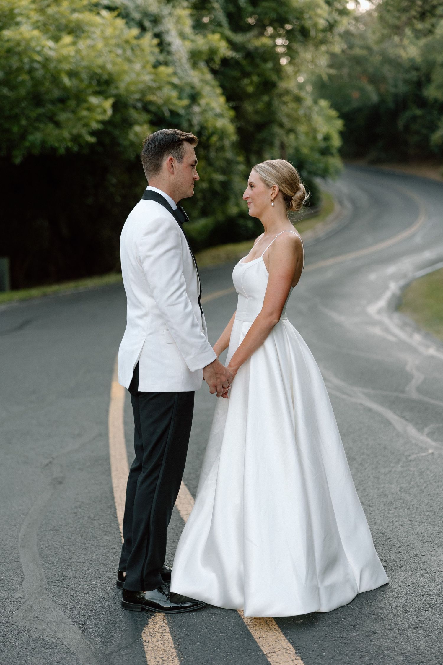 A couple in wedding attire stands together on a winding country road during their romantic outdoor photo session.
