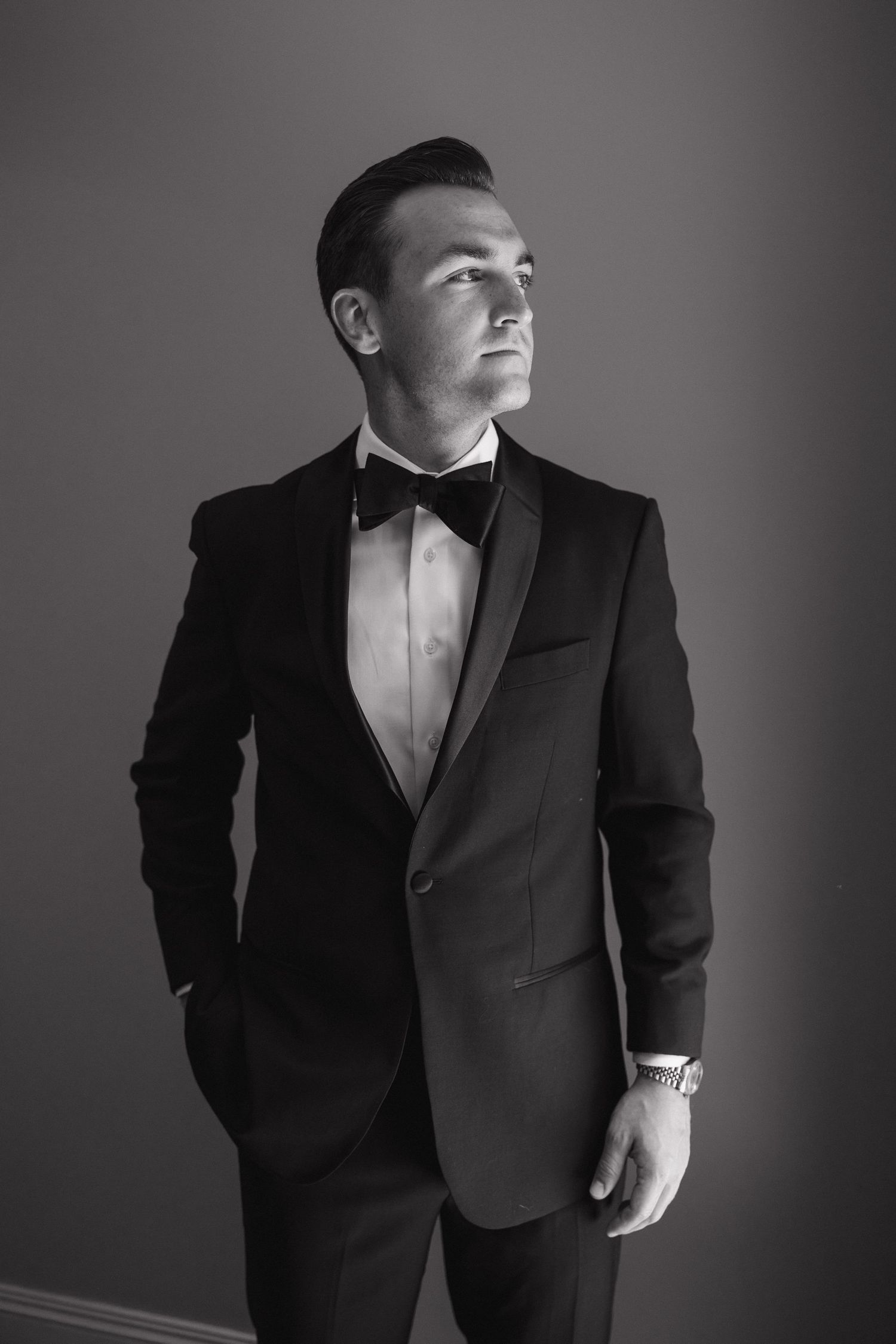 Black and white portrait series of a person in formal tuxedo attire striking dramatic poses against a dark background.