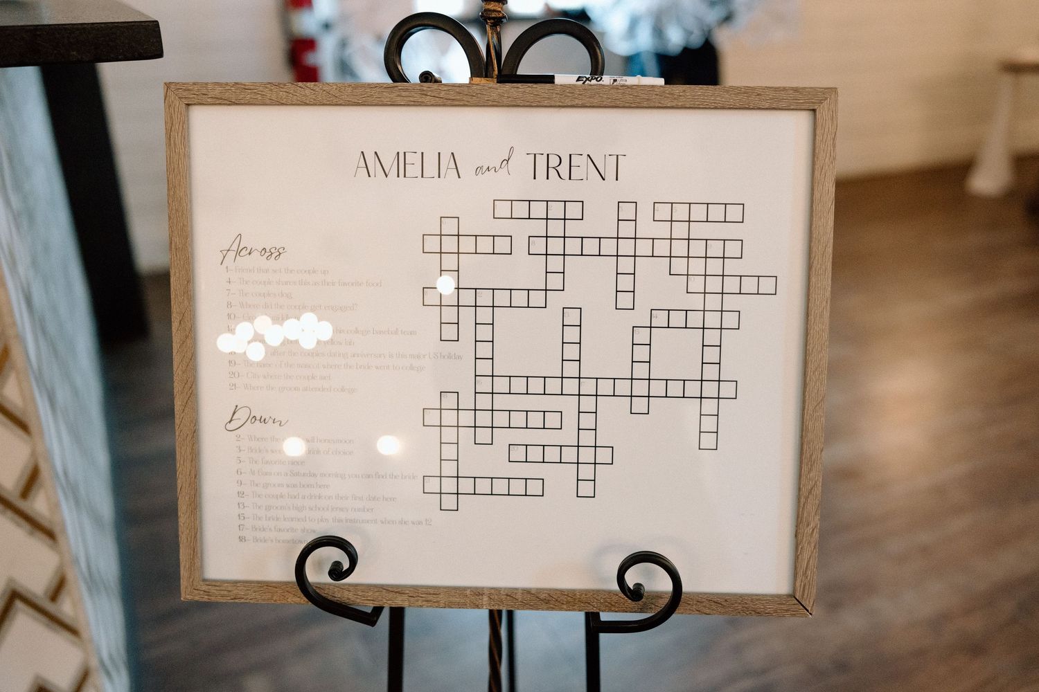 Elegant wedding reception table decor features a crossword puzzle card and ornate black metal stand against a soft blurred background.