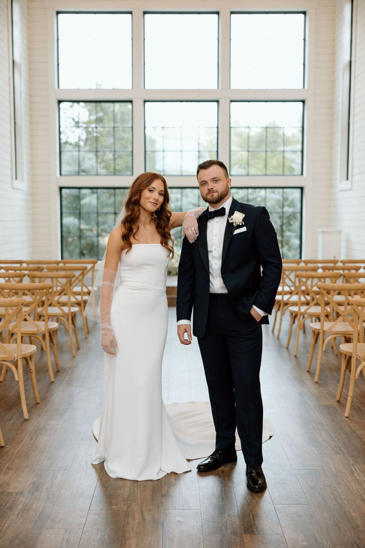 Couple shares romantic dance moves in bright indoor venue with wooden chairs and hardwood floors.