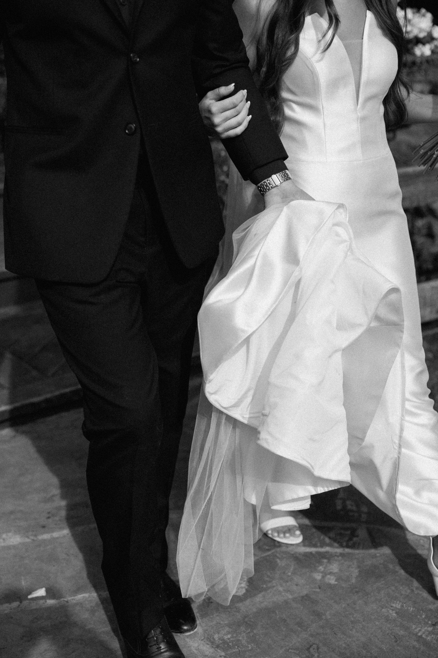 Black and white wedding photo series showing close-up details of a bride's white dress and groom's black suit while dancing.