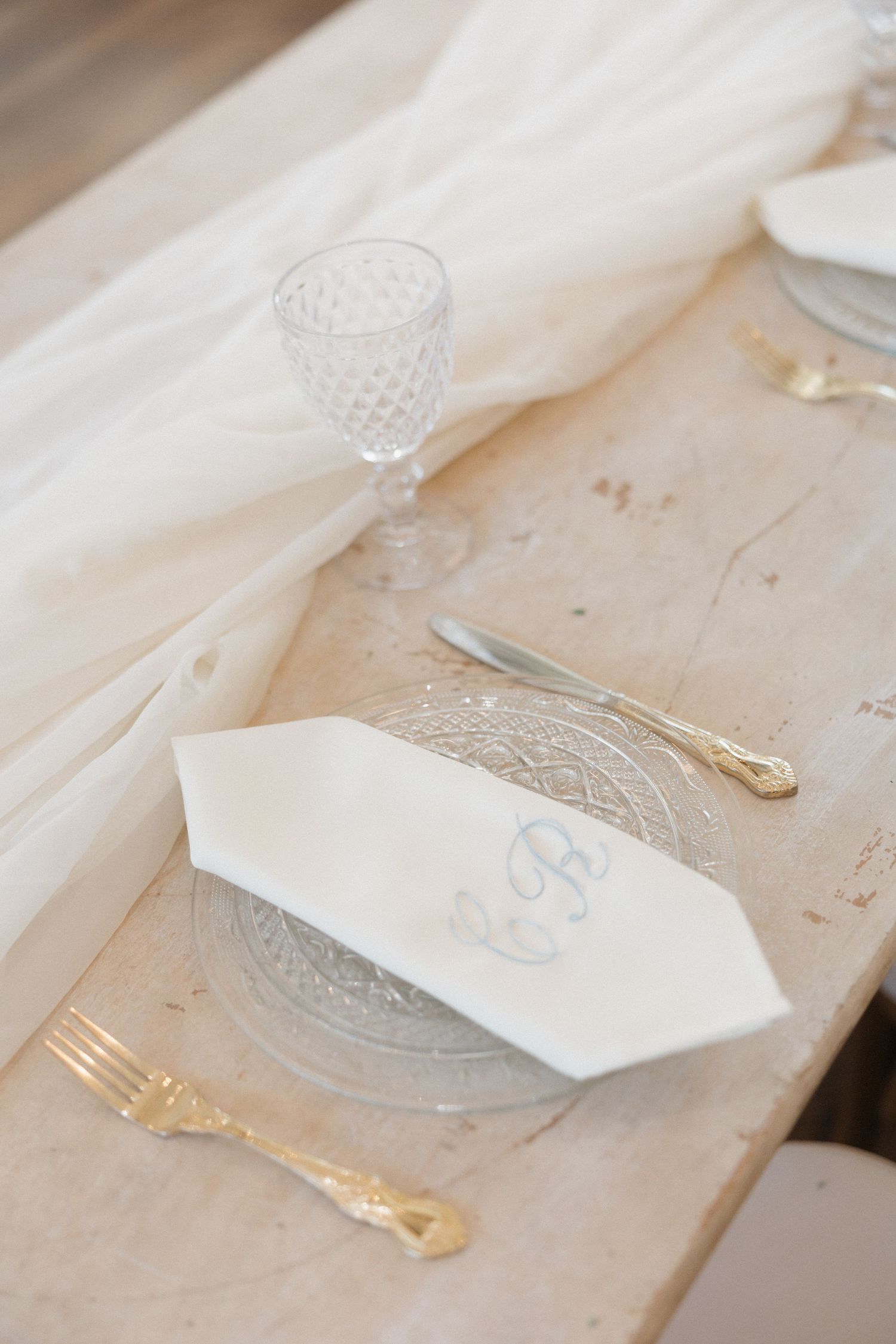 Elegant place settings with white linens and gold accents arranged on a light-colored table for a formal dining event.