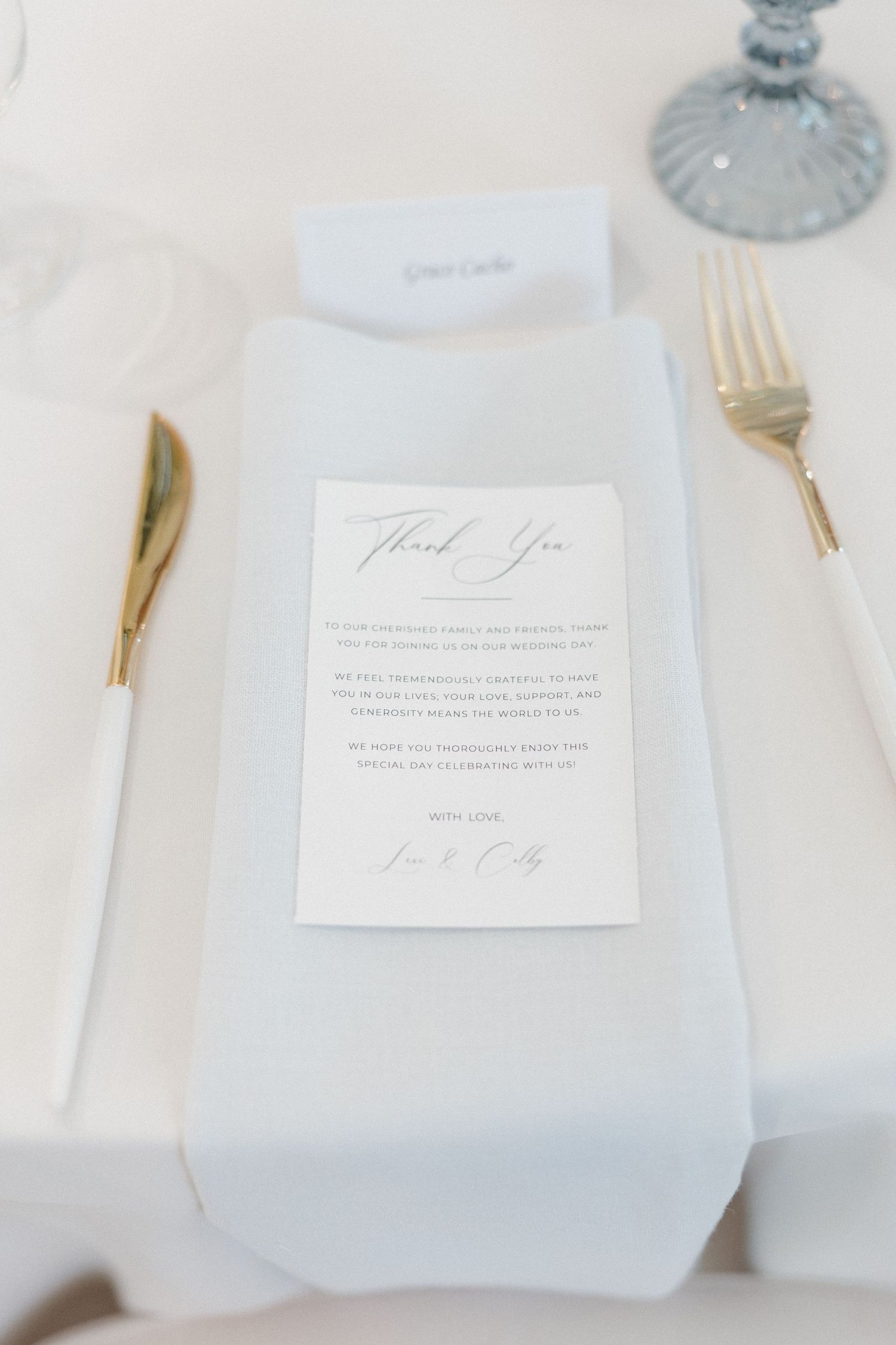 Elegant white place settings with gold cutlery and handwritten thank you notes create a sophisticated table arrangement.