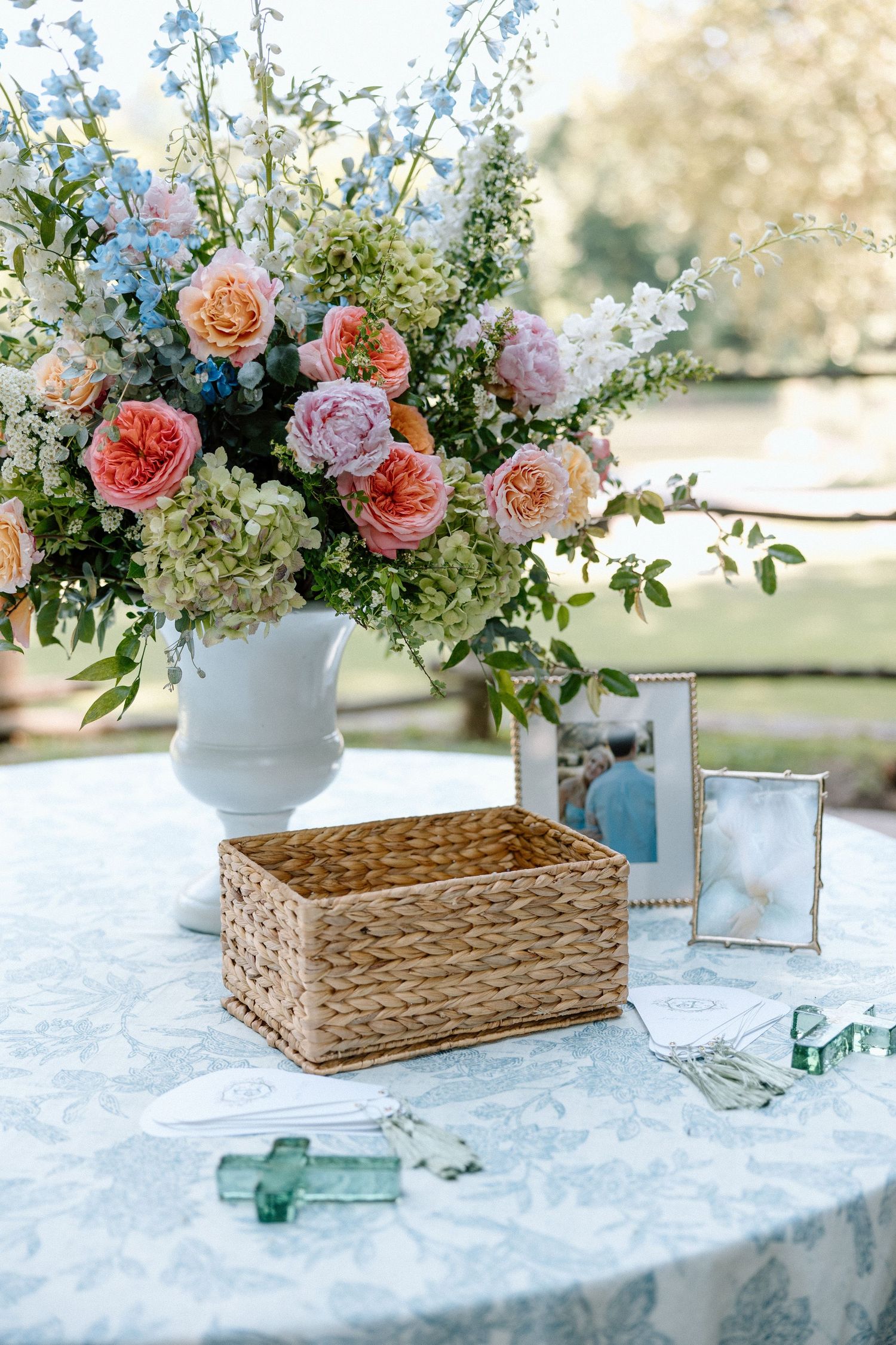 Elegant floral centerpieces with pink roses and greenery arranged beside woven baskets on a white lace tablecloth.