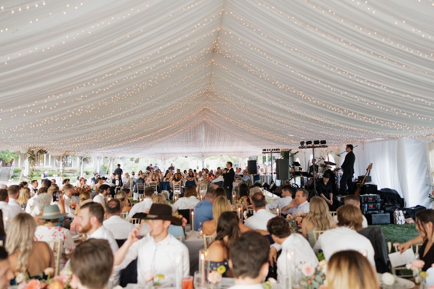 A panoramic view of guests dining and socializing under an elegant white tent at an outdoor wedding reception.
