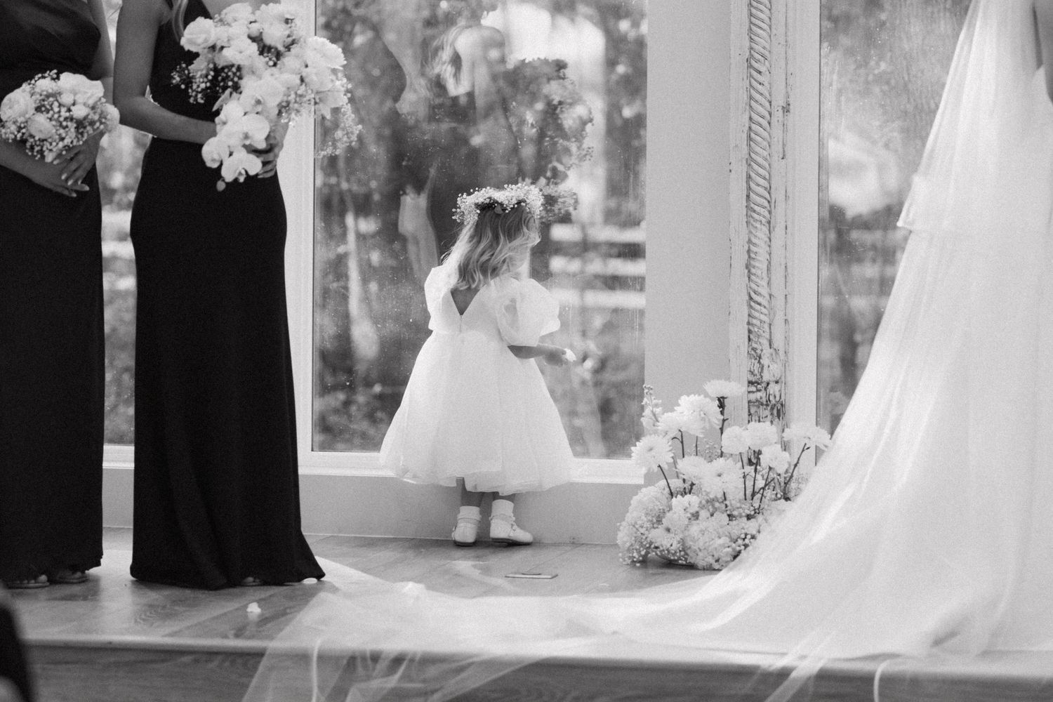 A wedding couple stands together in formal attire while guests gather around them during an outdoor ceremony.
