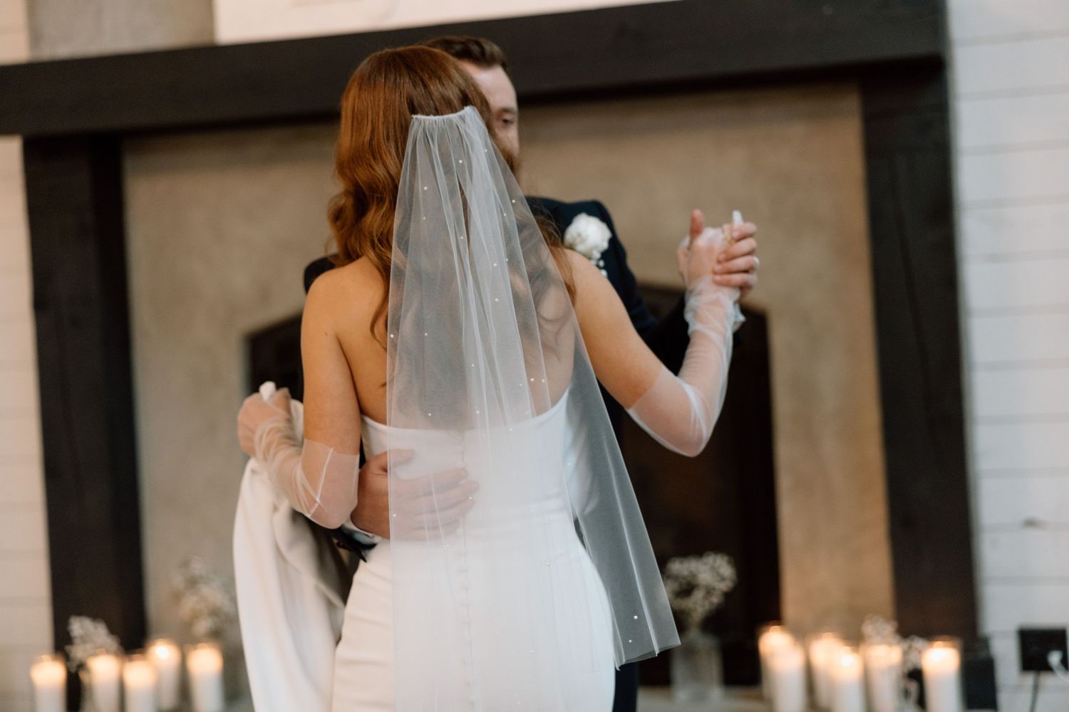A bride in a white wedding dress and veil raises her hand while dancing at an indoor reception venue.